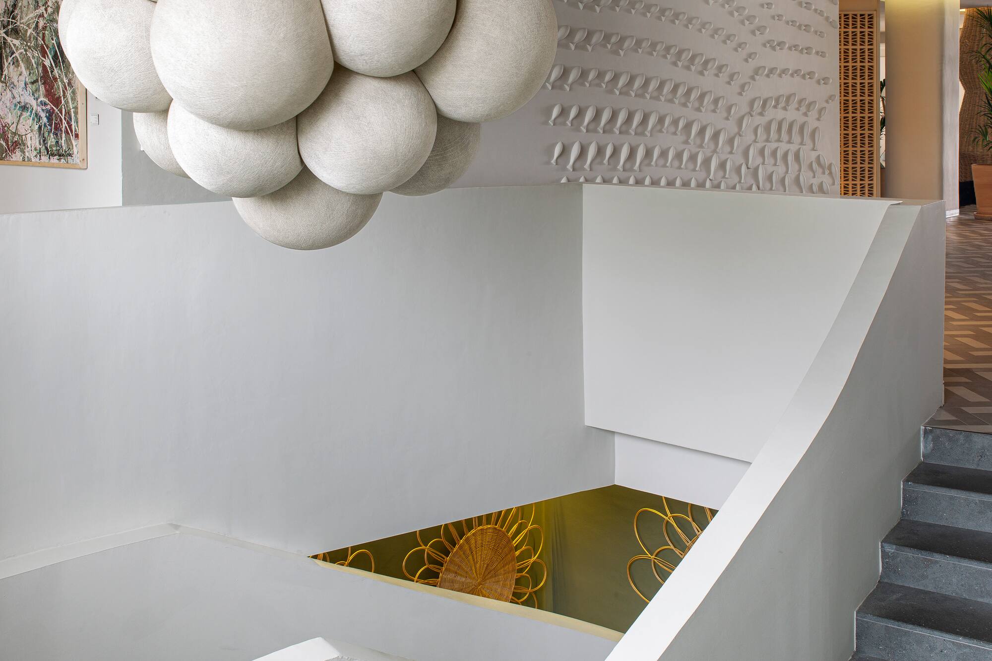 Modern interior with white bubble chandelier, grey staircase, and sculptural wall.