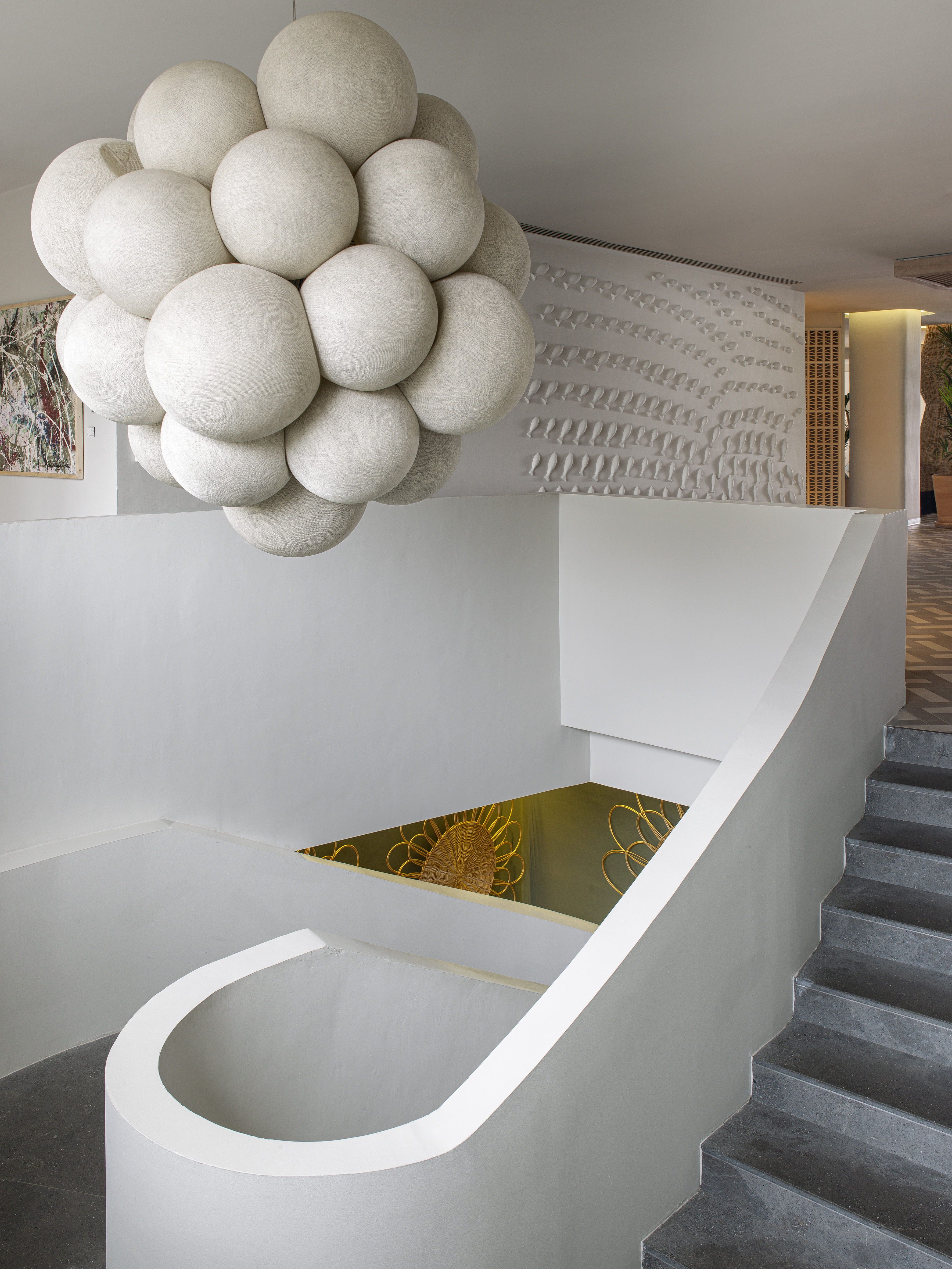 Modern interior with white bubble chandelier, grey staircase, and sculptural wall.