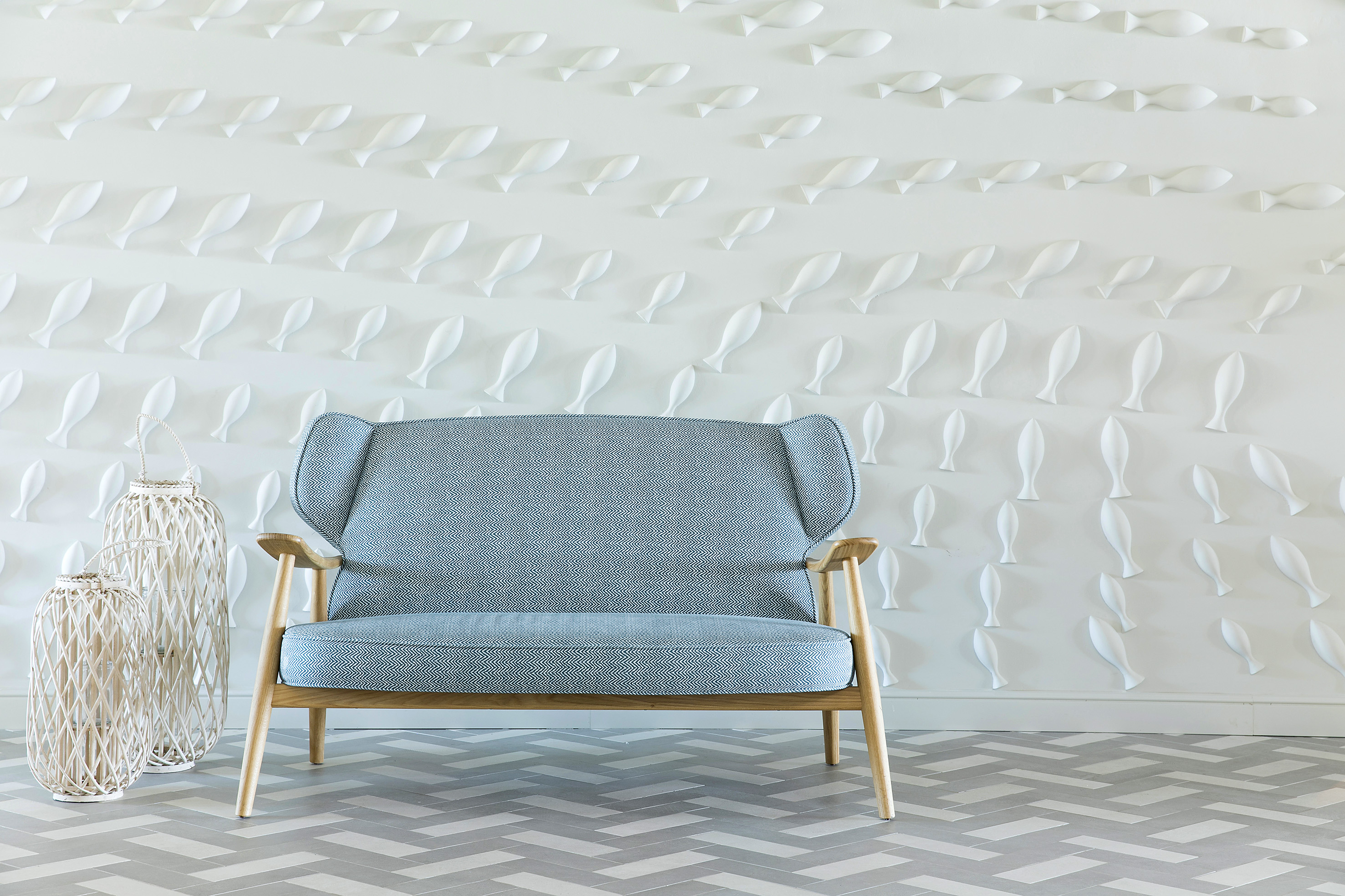 Blue armchair, white 3D fish wall decor, wicker lanterns, herringbone floor.