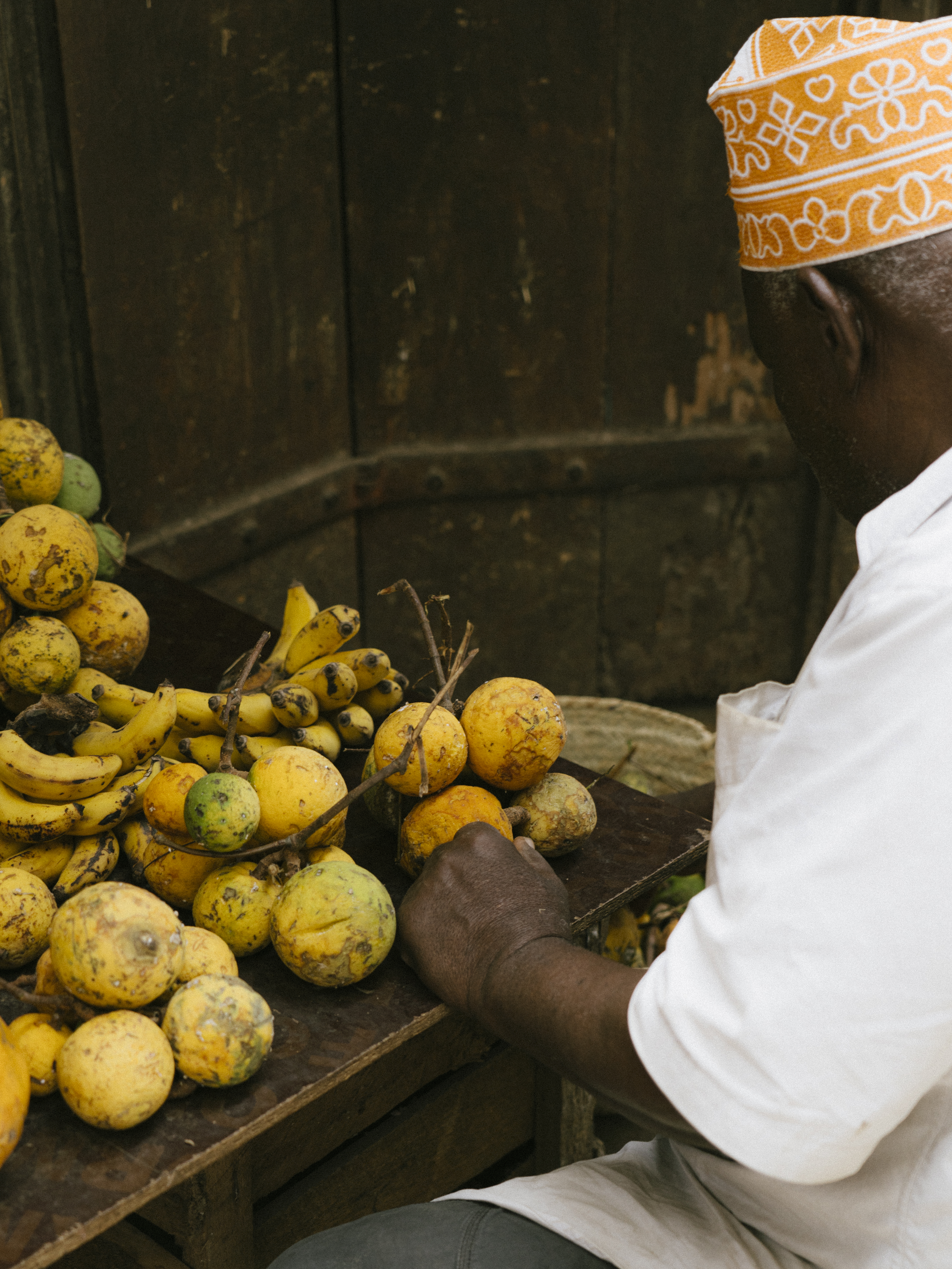 Market vendor in orange cap sorting tropical fruit and bananas.