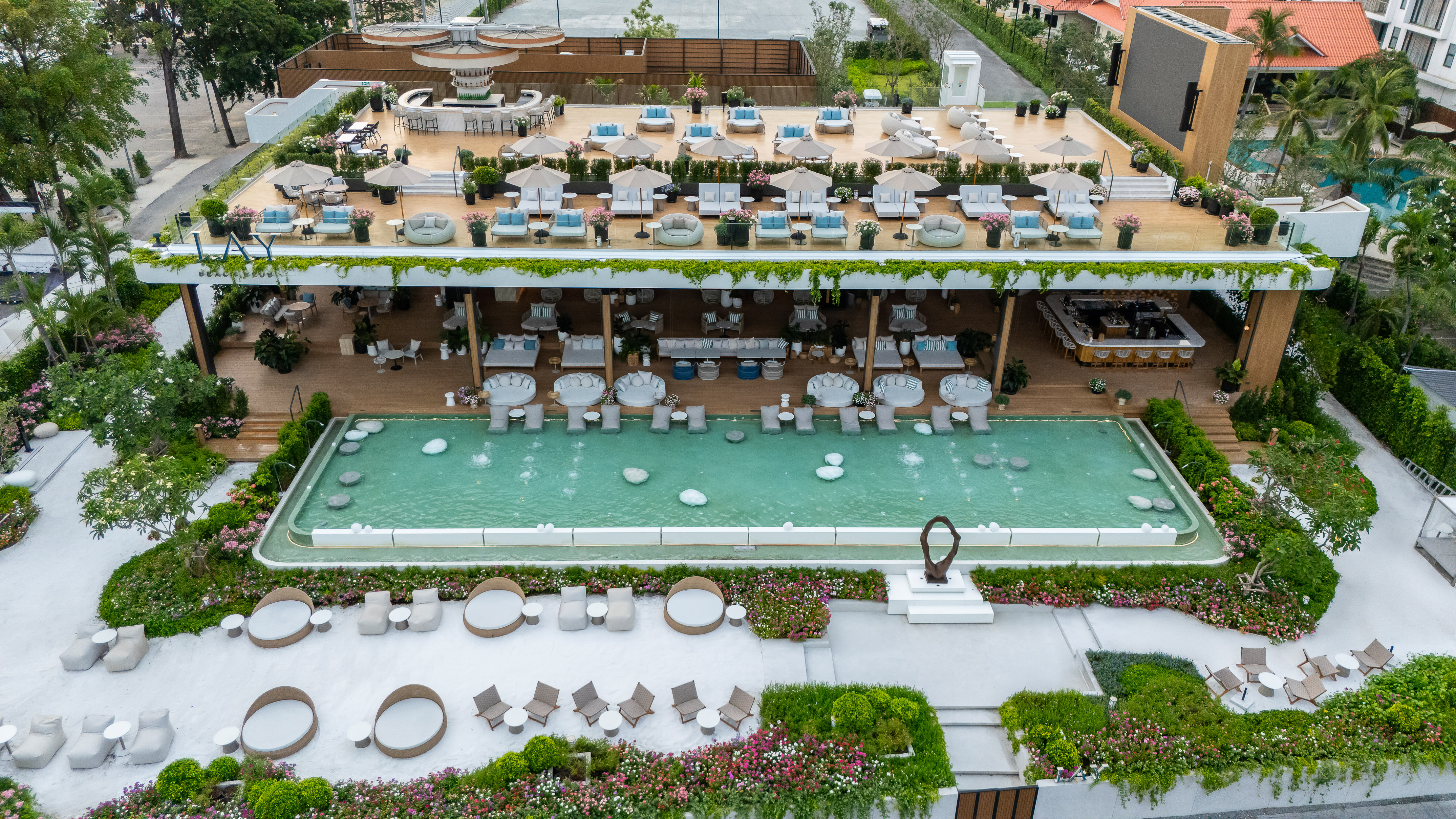 Modern multi-level beach club with rooftop lounge, swimming pool, bar, and lush gardens.