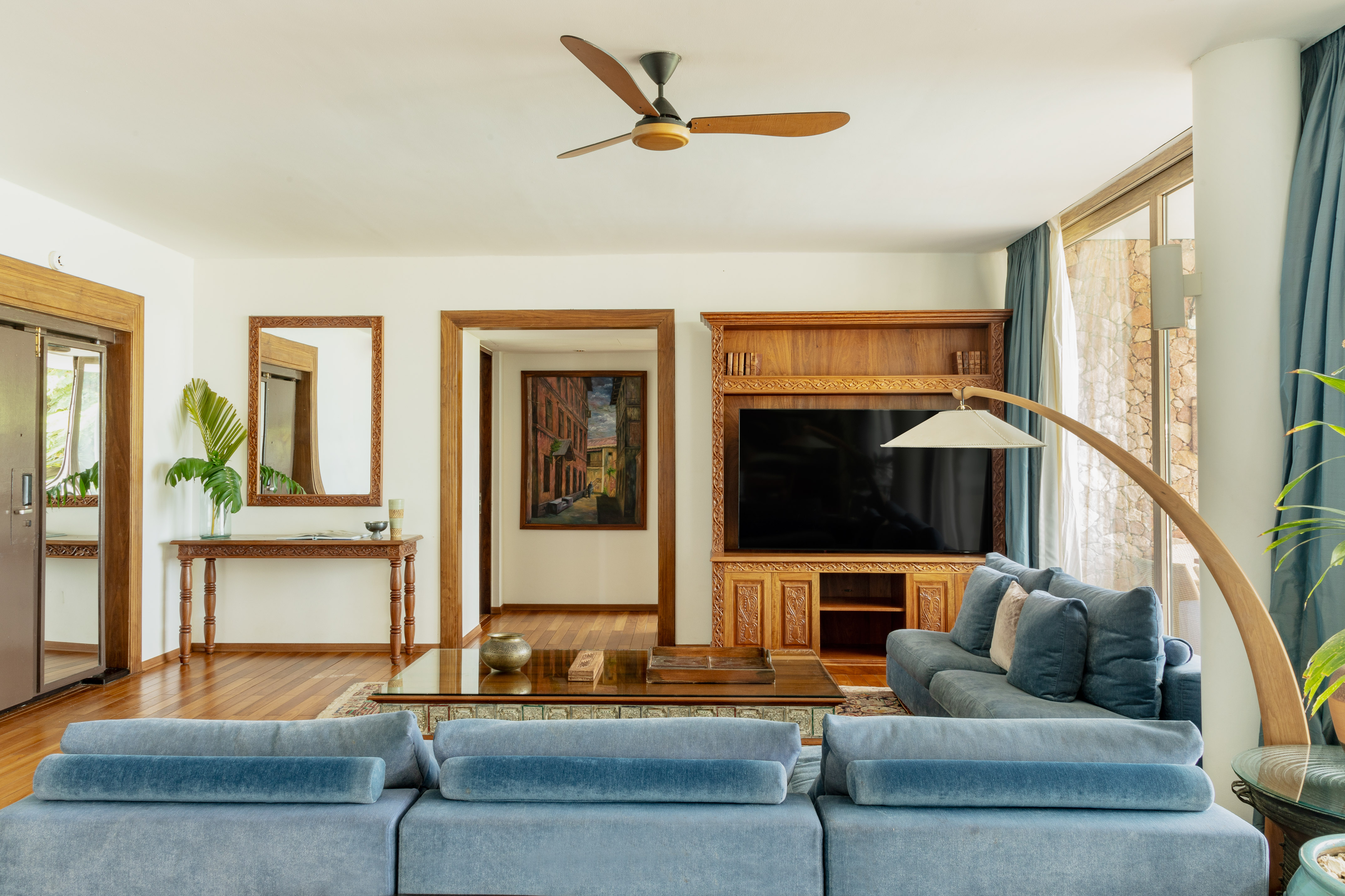 Luxury living room with blue velvet sofas, wood trim, TV, and ceiling fan.