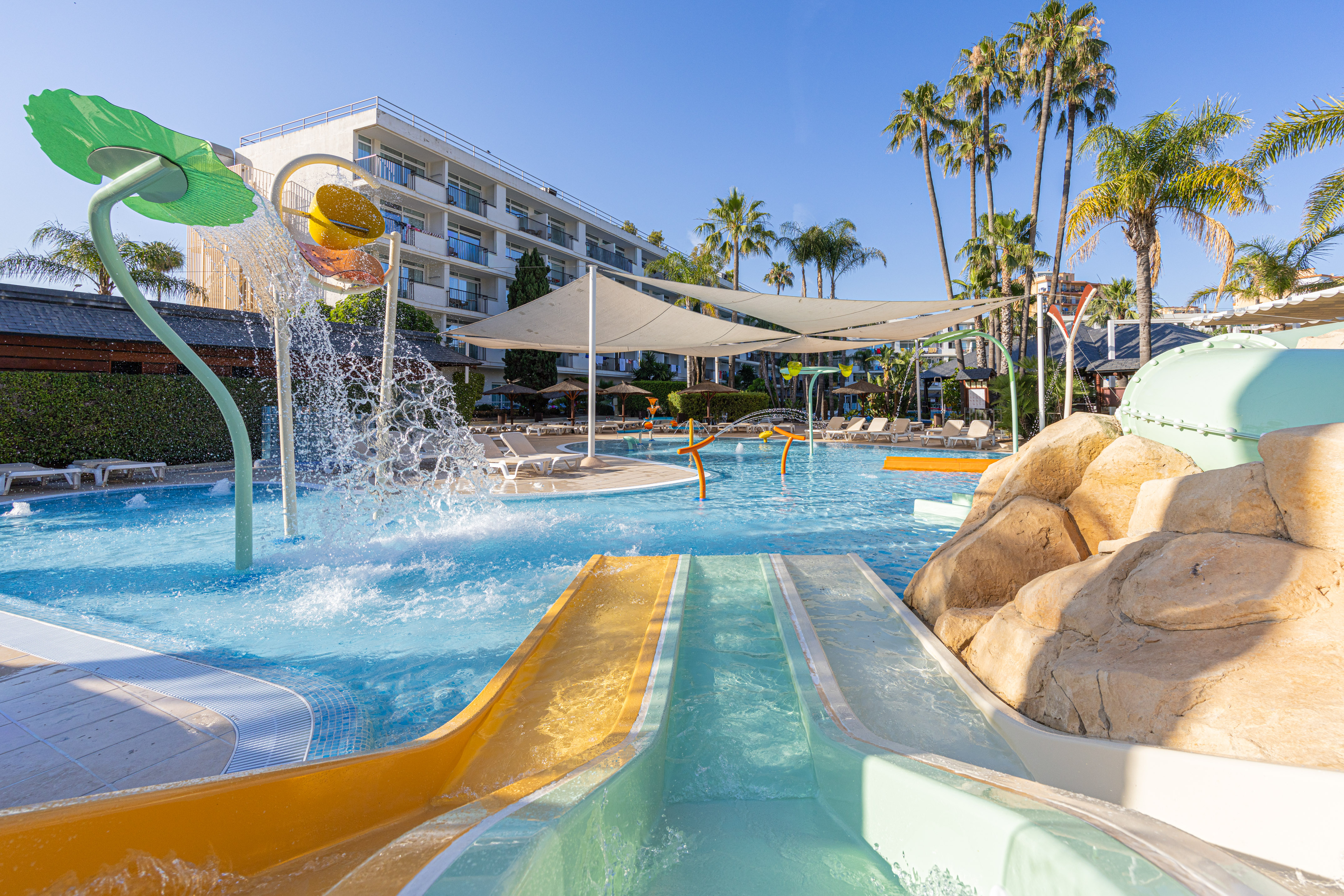 Hotel water park with colorful slides, splash pad, and palm trees.