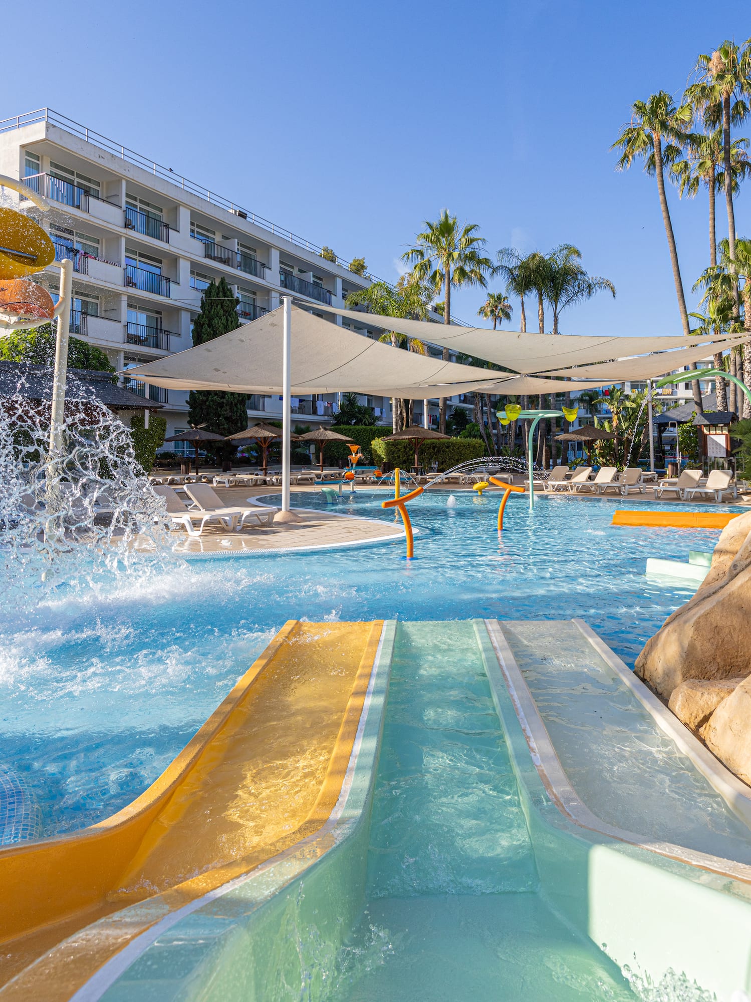 Hotel water park with colorful slides, splash pad, and palm trees.