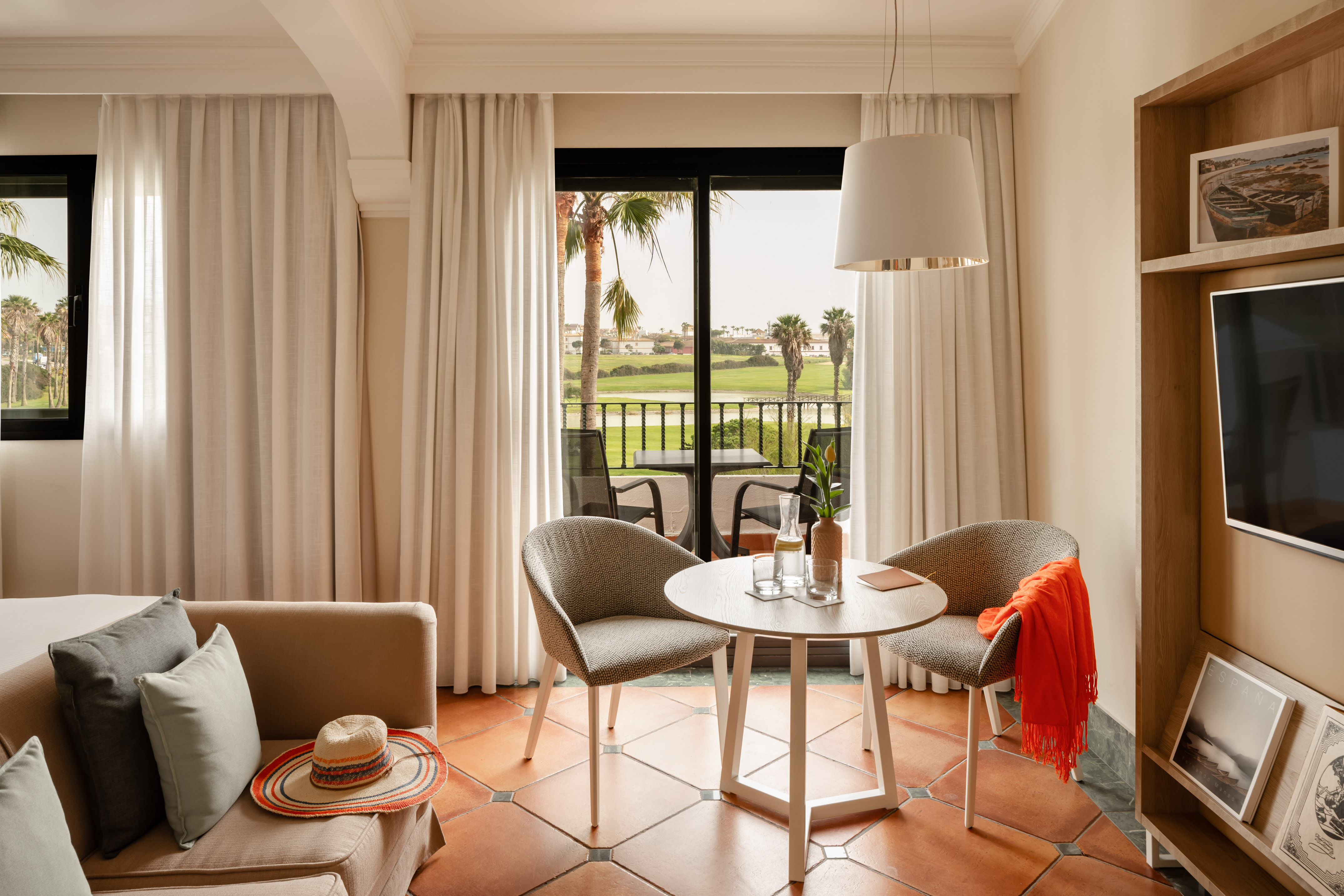 Modern hotel suite living area overlooking golf course from balcony, cozy seating.