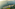 Aerial of coastal resort, high-rise hotel, villas, ocean, and green mountains.