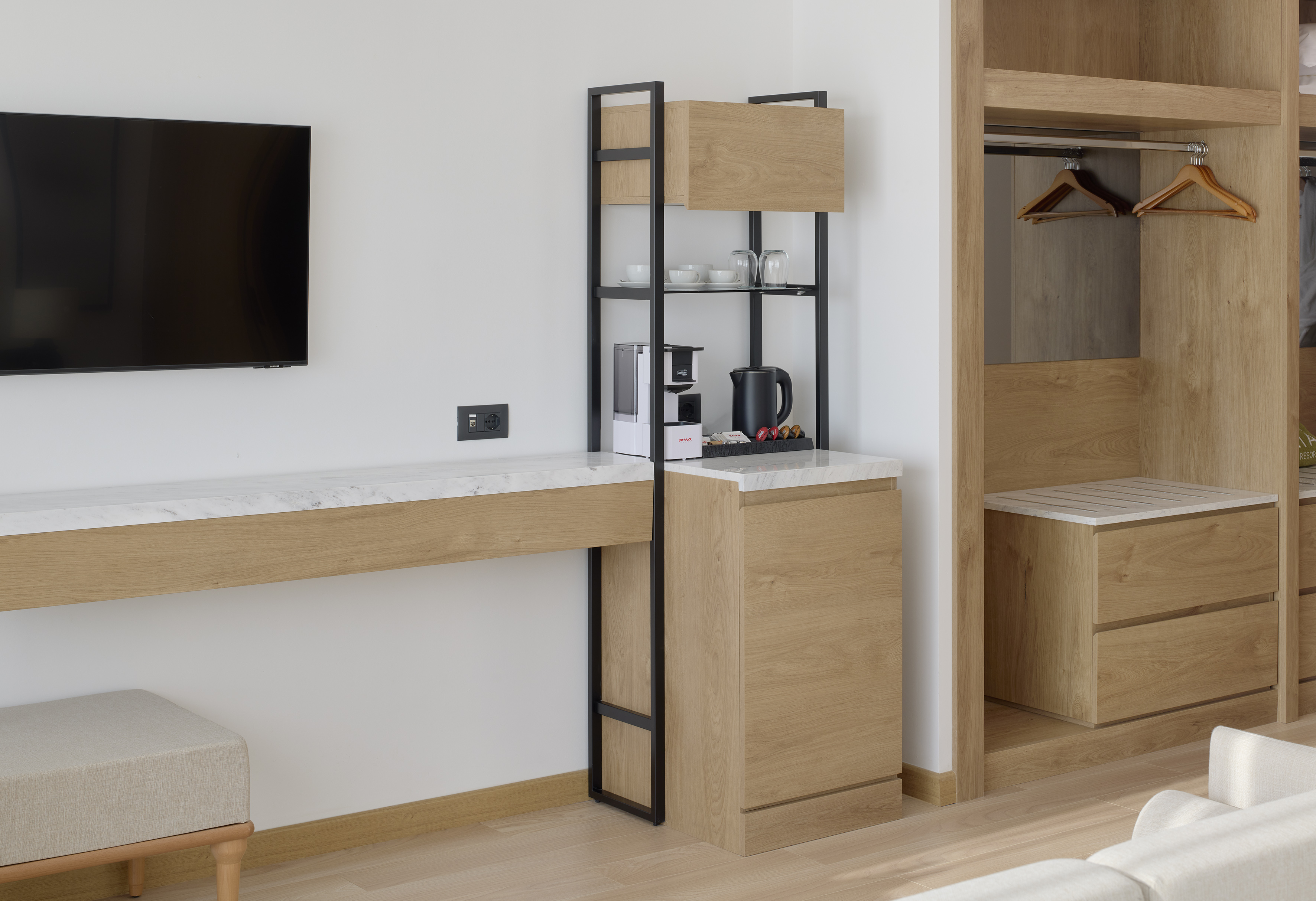 Modern hotel room with TV, marble desk, coffee station, and wooden closet.