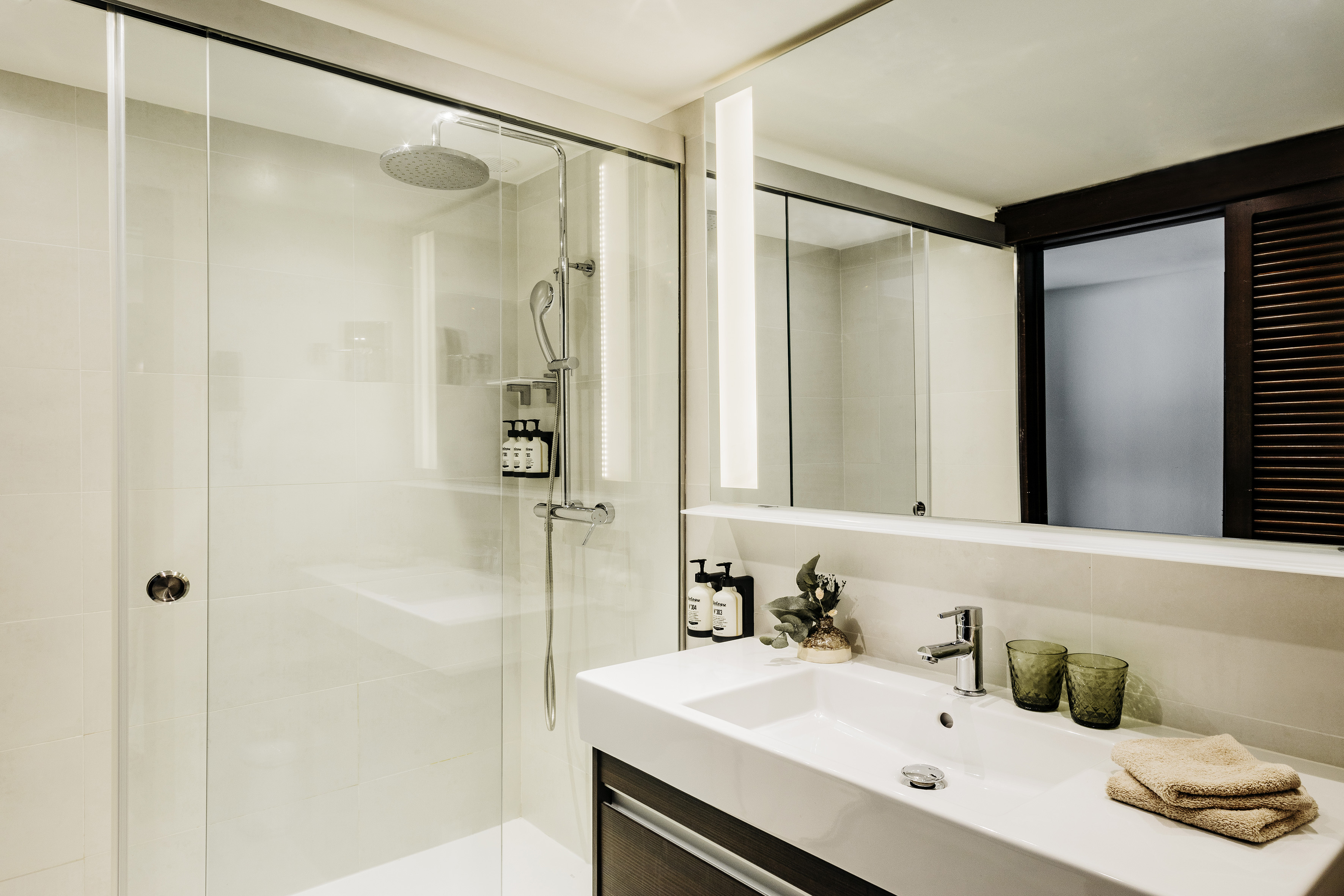 Modern bathroom with glass shower, white vanity, mirror with LED lights.