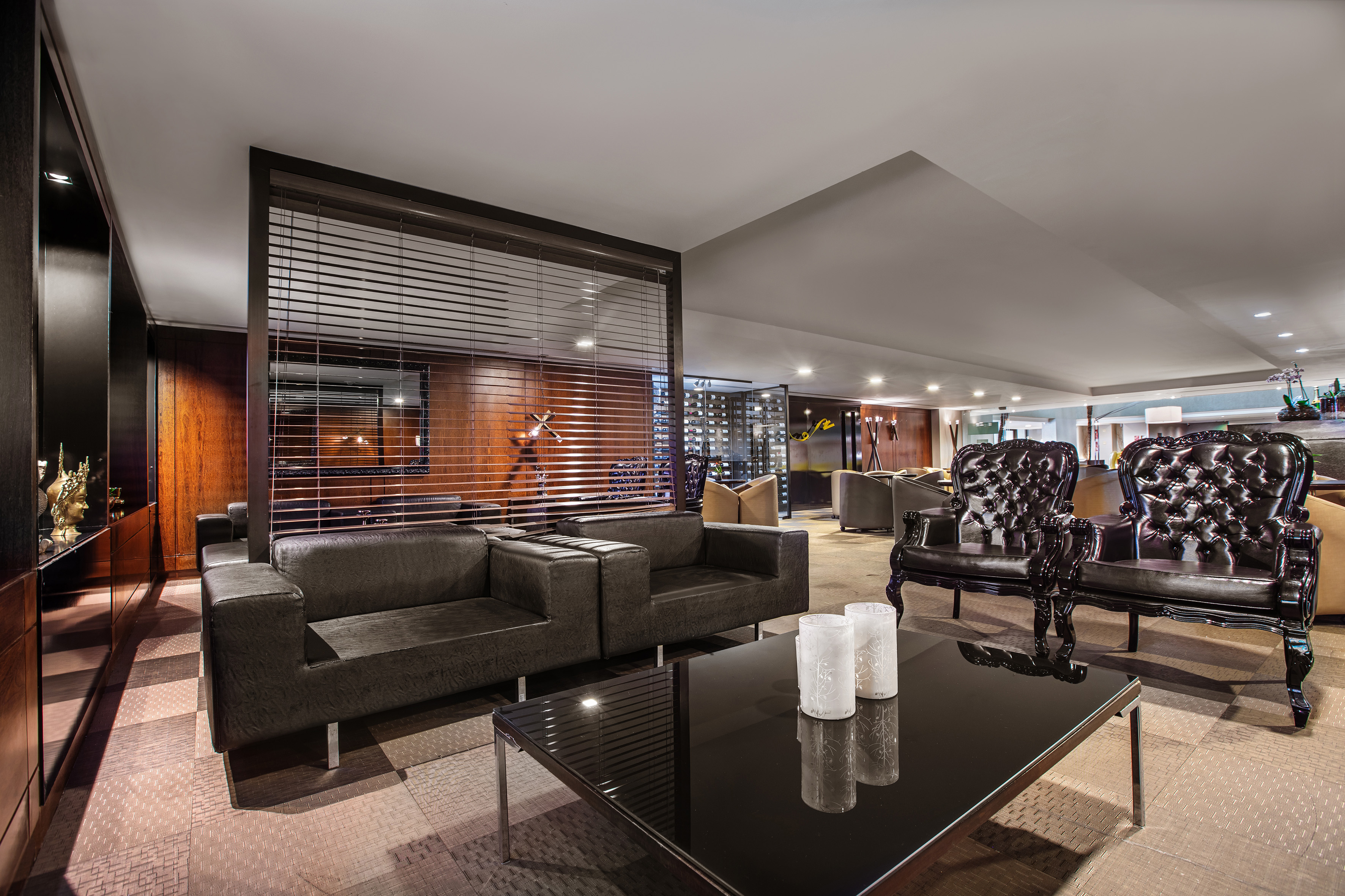 Upscale lounge with dark leather sofas, tufted chairs, glass table, and wood divider.