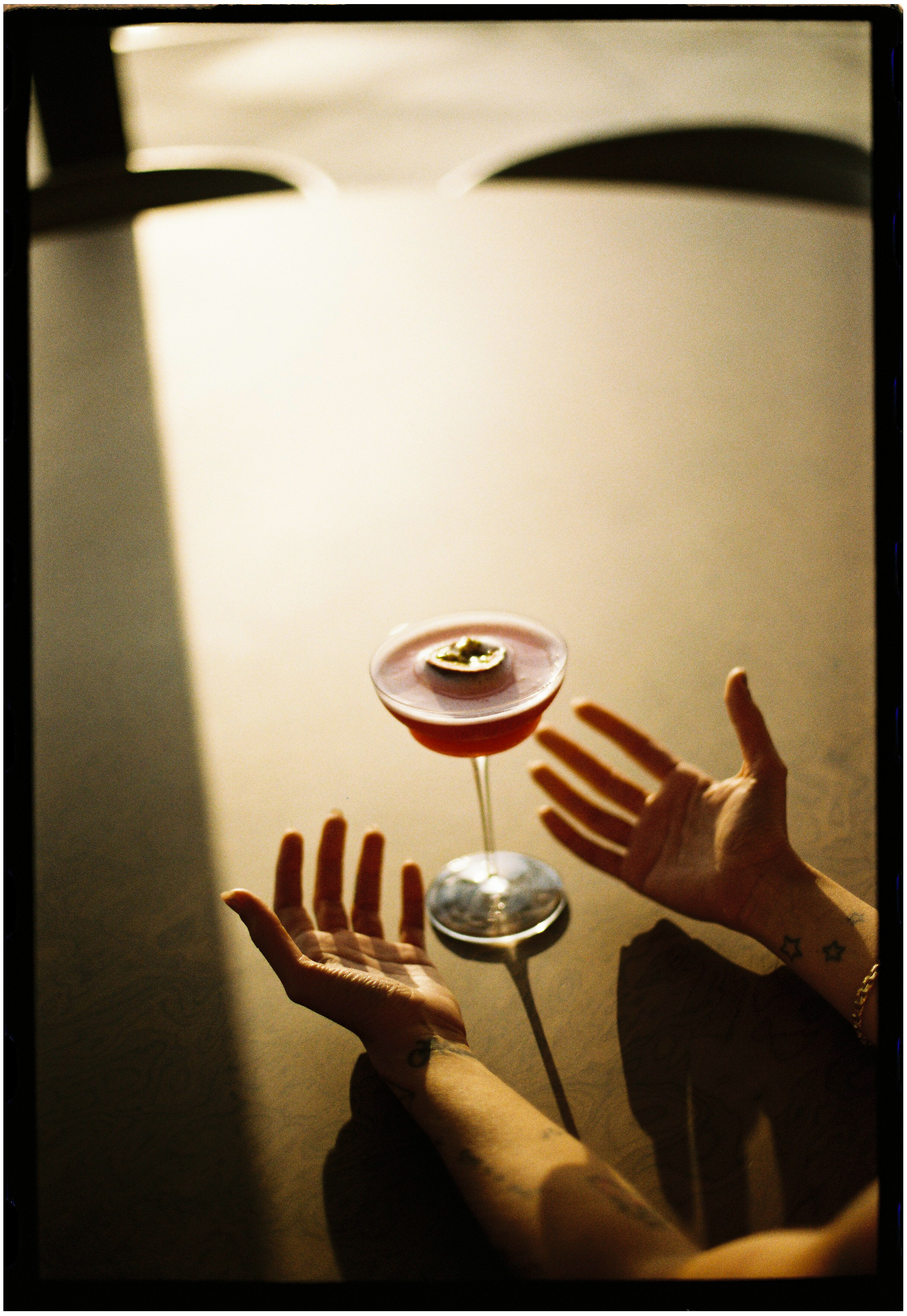 Pink passion fruit martini cocktail between open hands on a shadowed table.