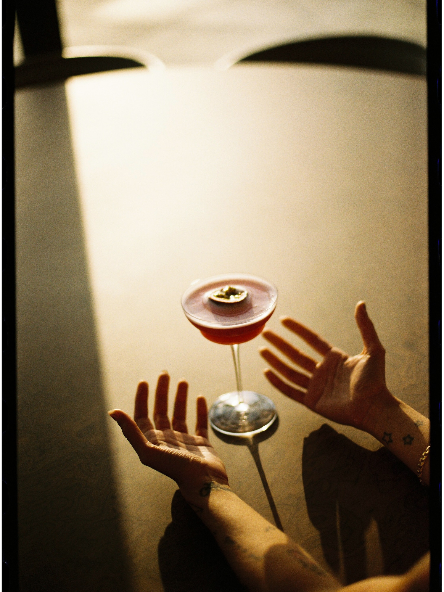 Pink passion fruit martini cocktail between open hands on a shadowed table.