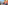 Sunny hotel balcony with chairs, coffee, overlooking resort pool and palm trees.