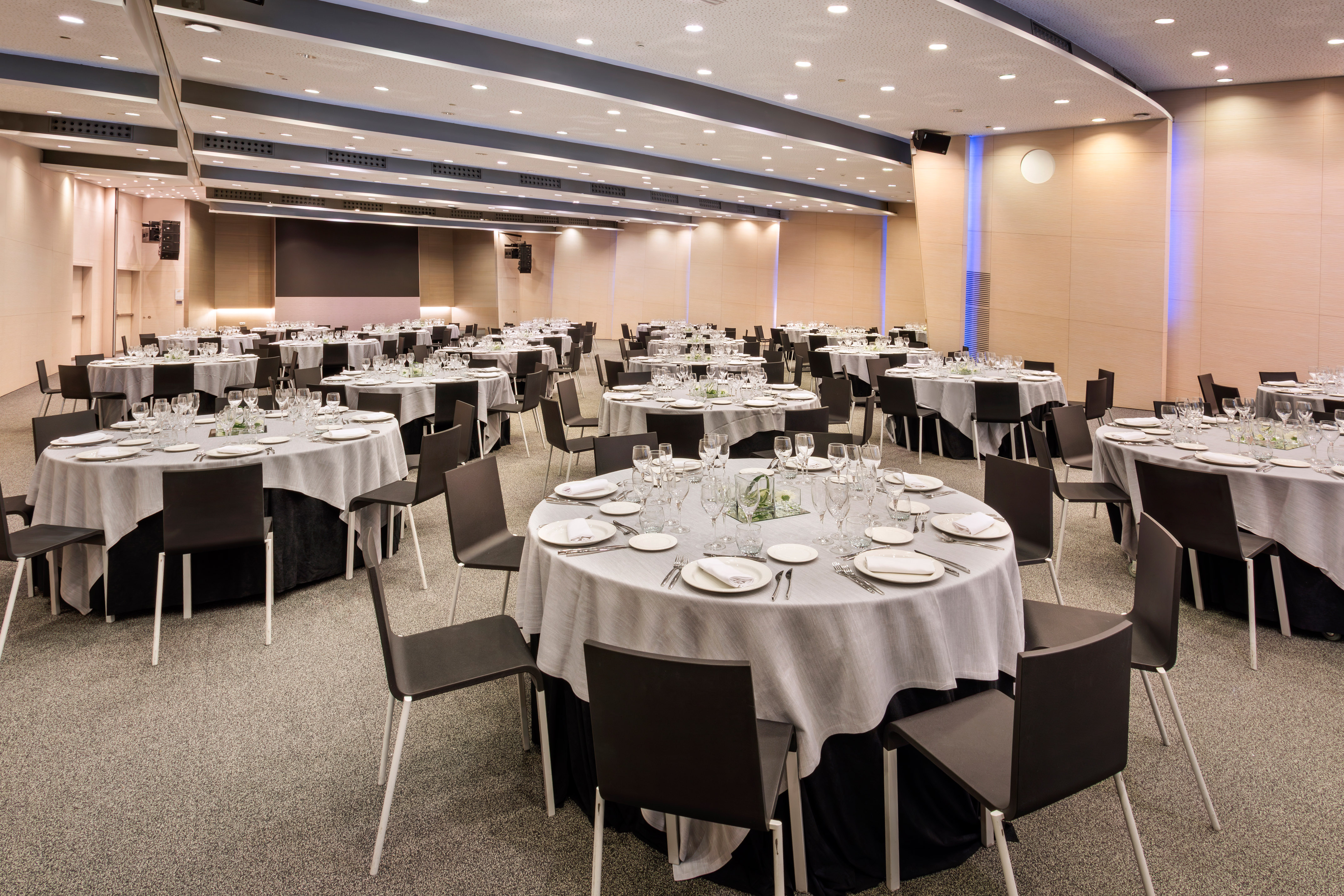 Modern banquet hall with round tables set for dining and contemporary decor.