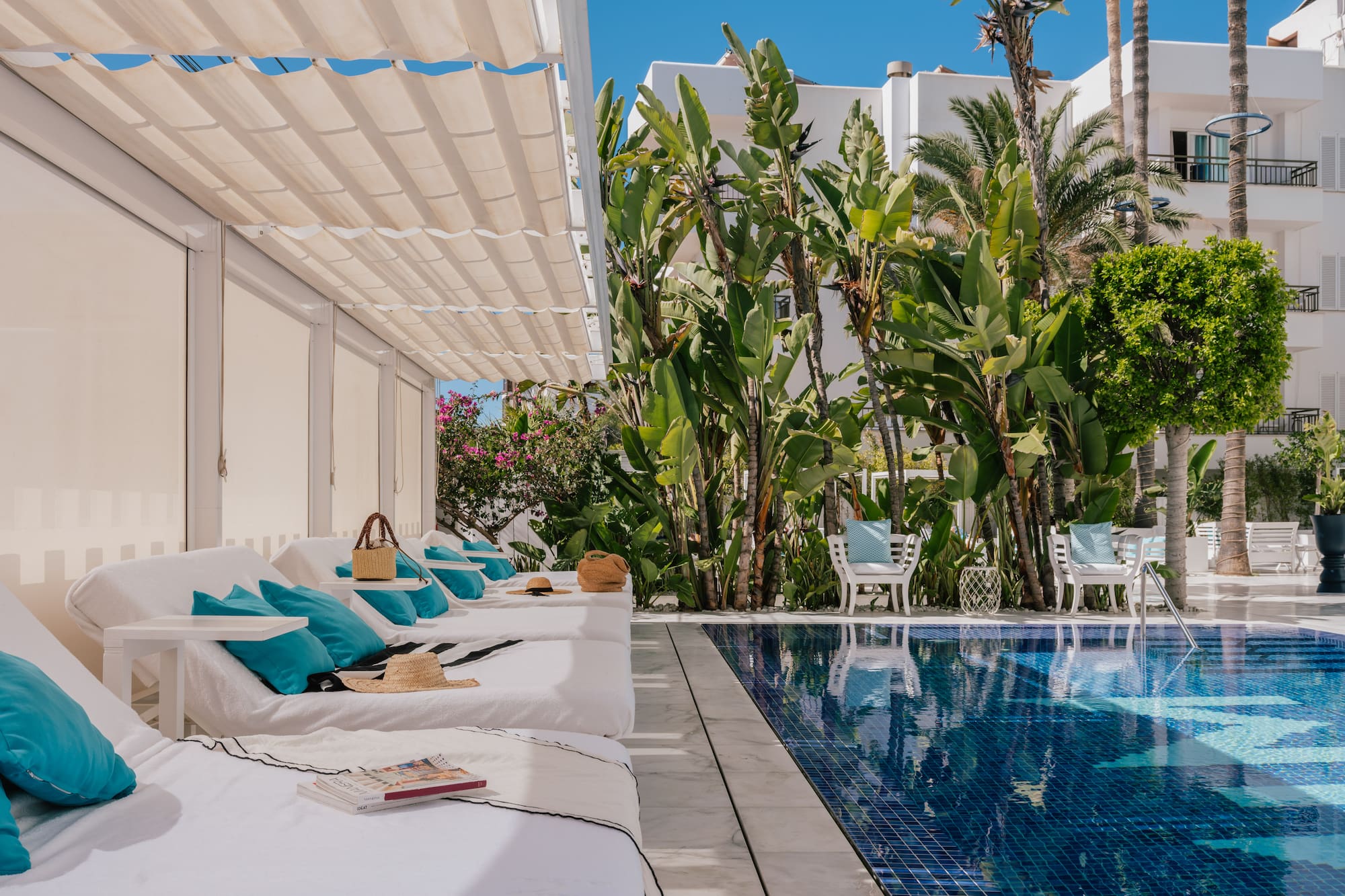 Luxury resort poolside with white daybeds, blue tiled pool, and tropical landscaping.