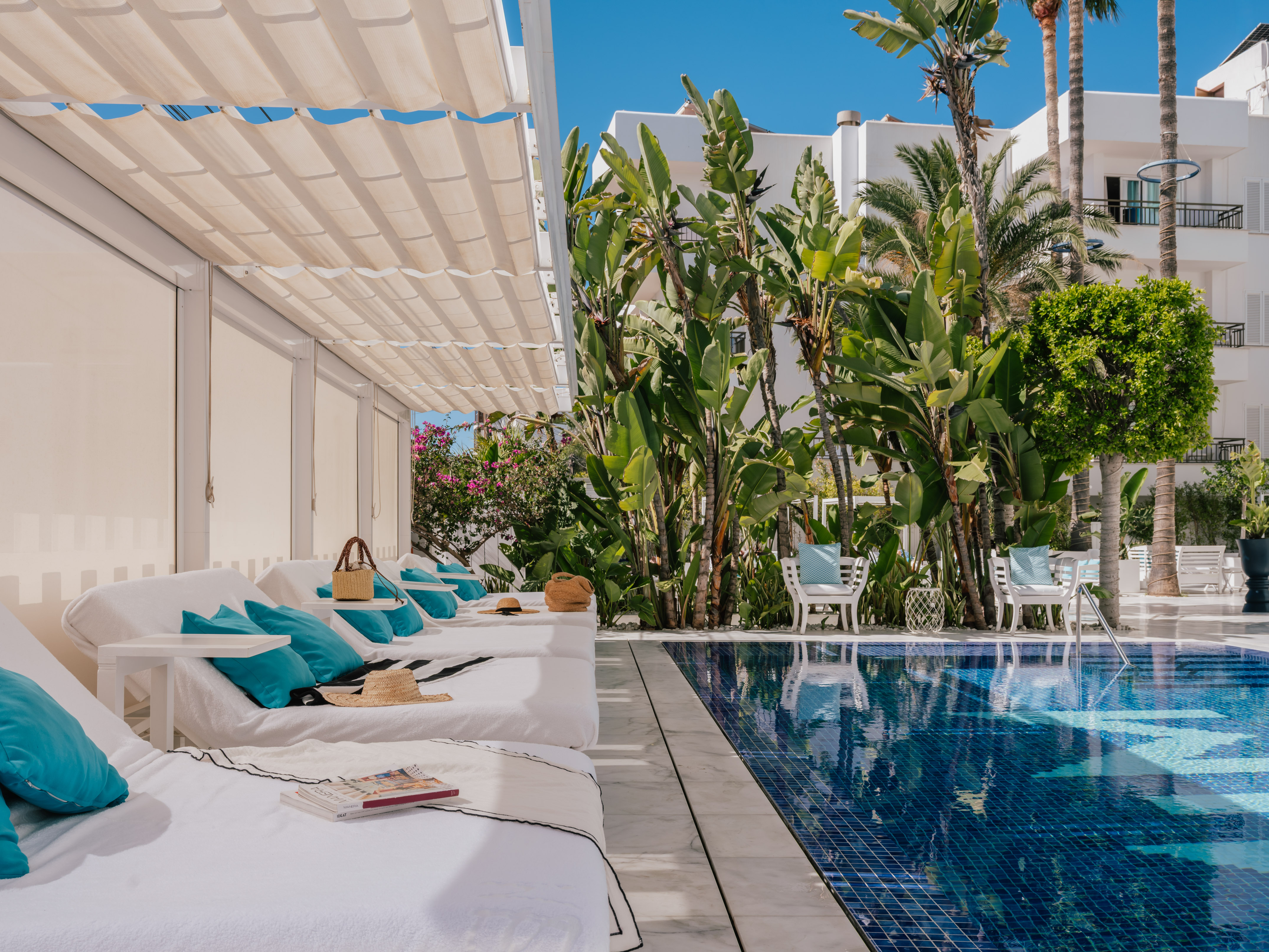 Luxury resort poolside with white daybeds, blue tiled pool, and tropical landscaping.