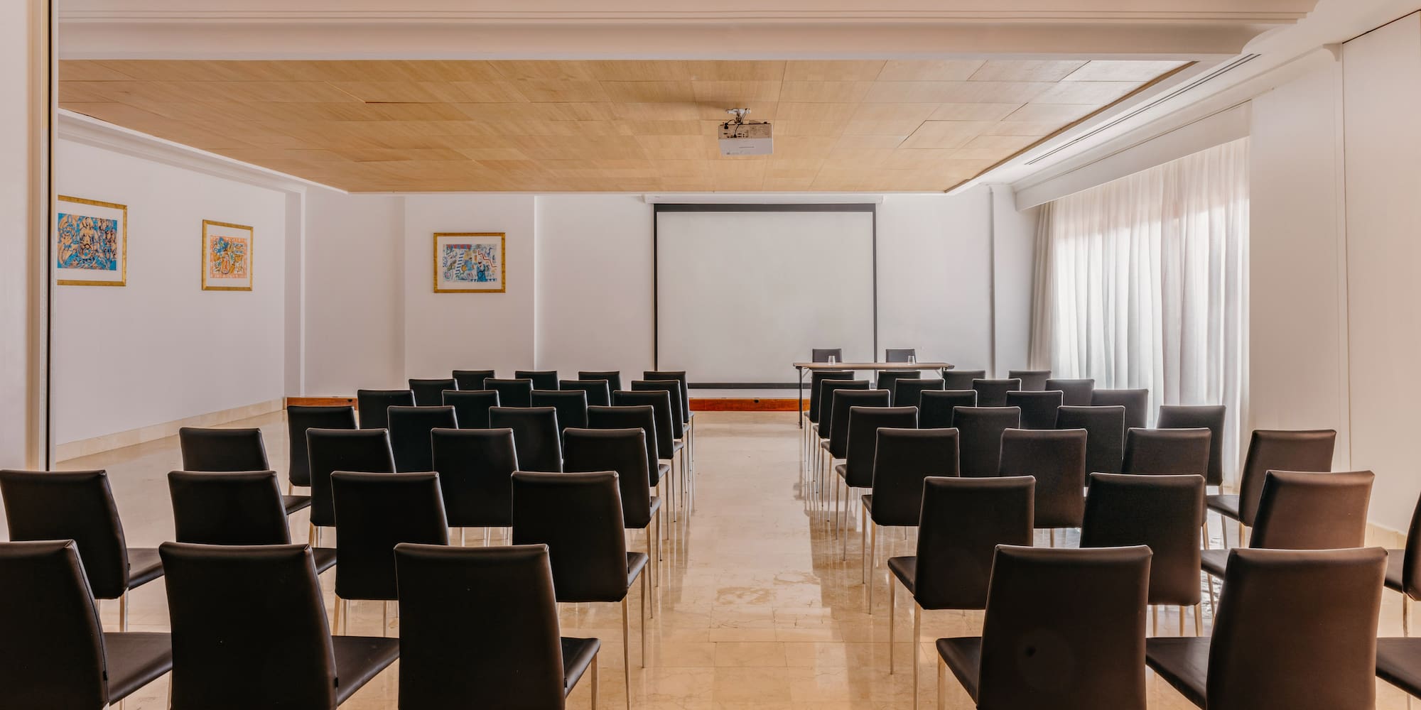 Spacious conference room with projector, screen, and black chairs.