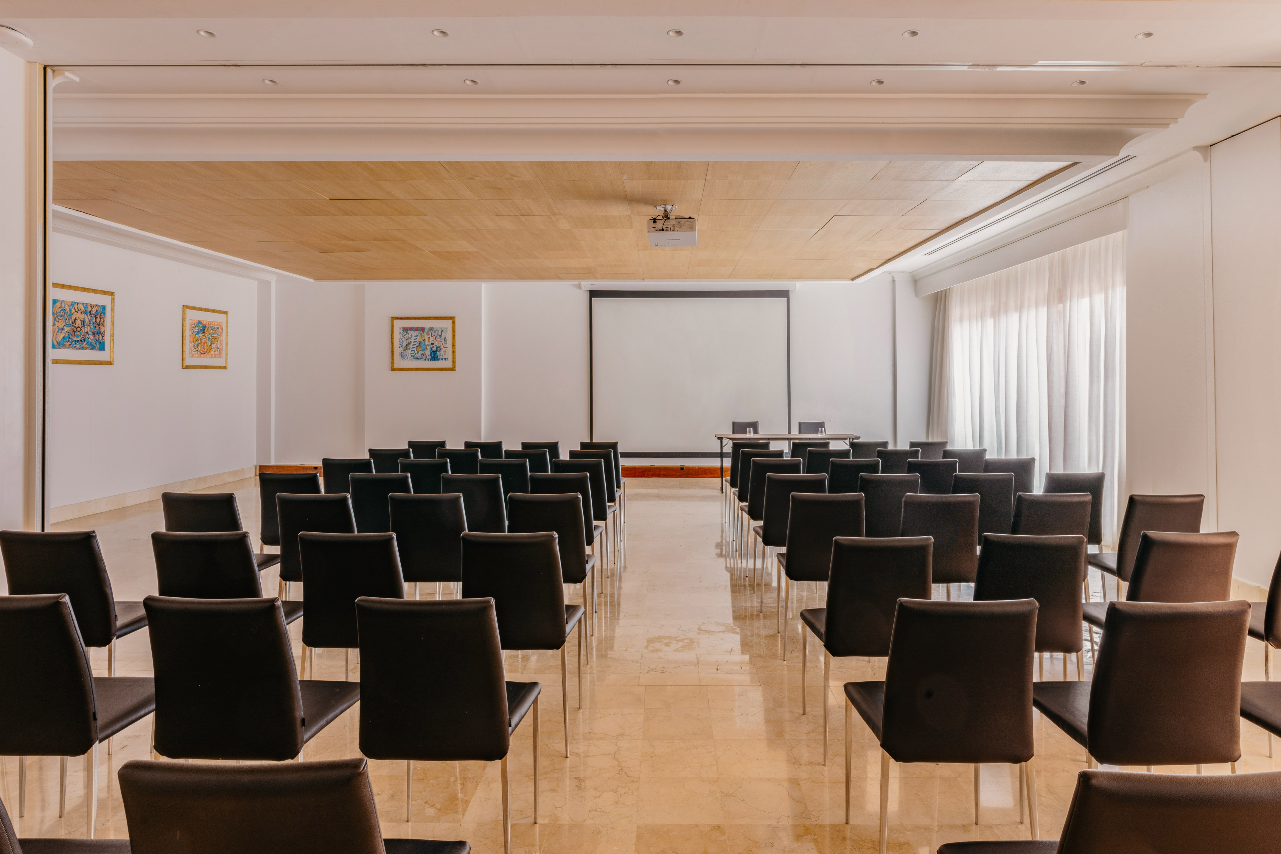 Spacious conference room with projector, screen, and black chairs.