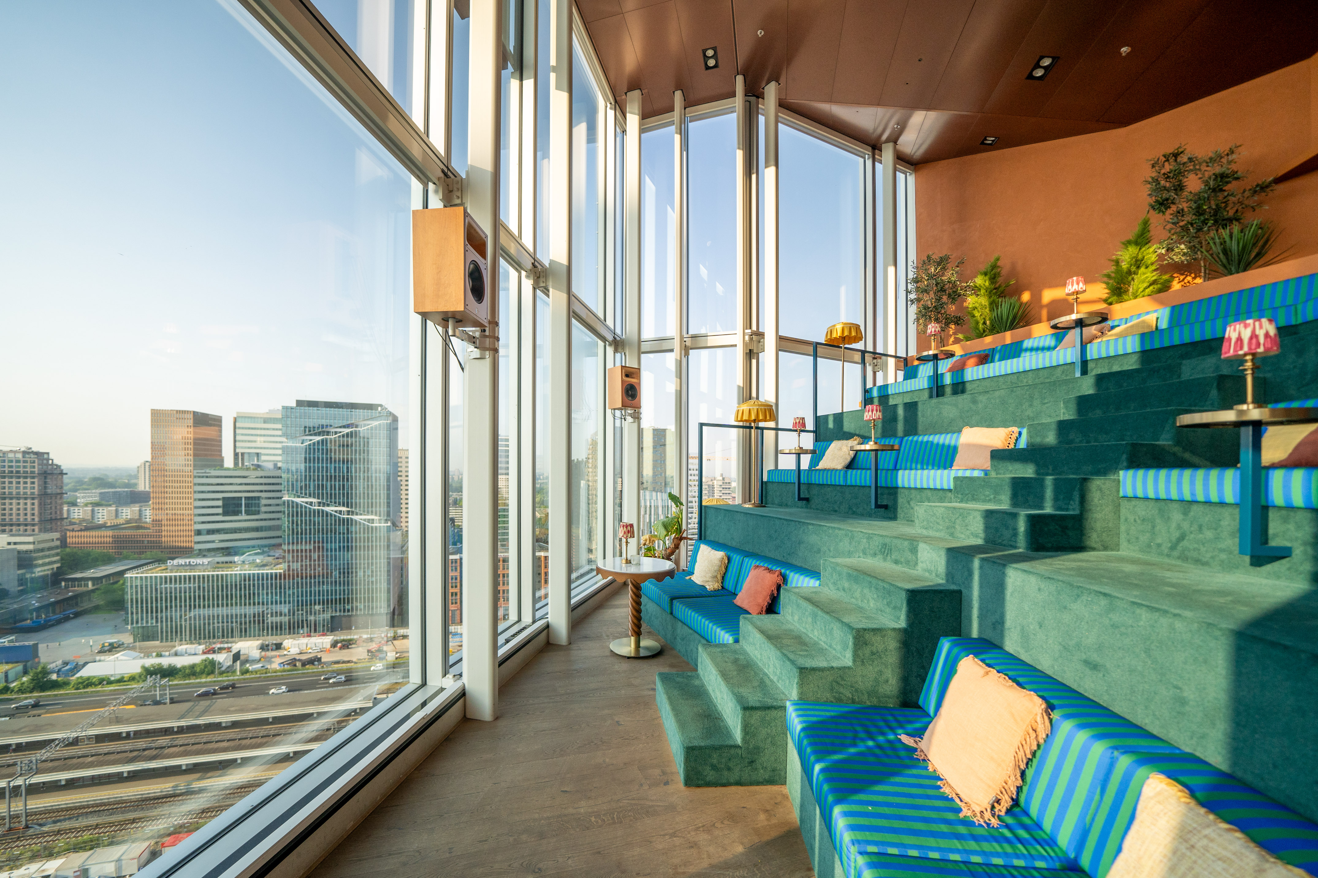 Modern tiered lounge, city panorama, large windows, and green seating.