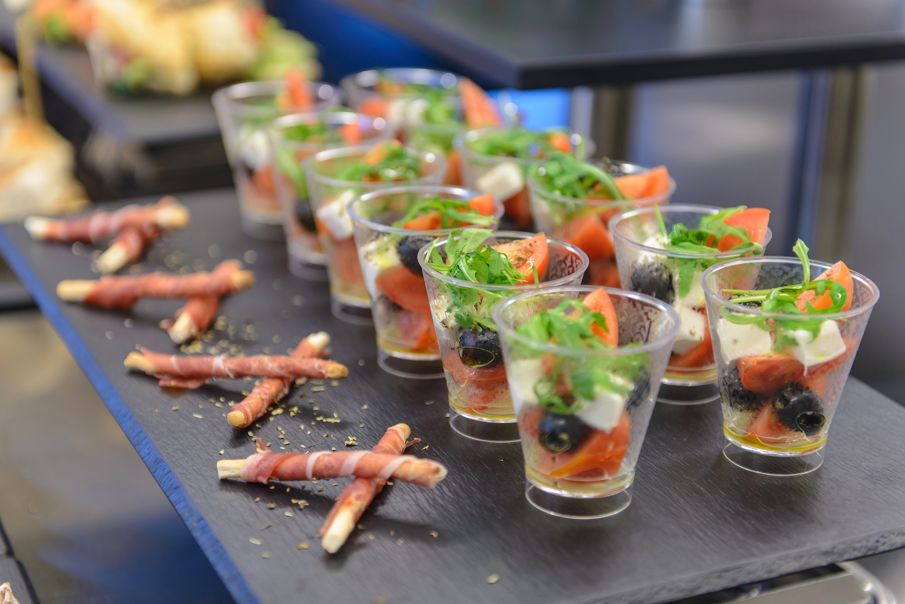 Mini Caprese salad cups and prosciutto-wrapped breadsticks on a catering tray.