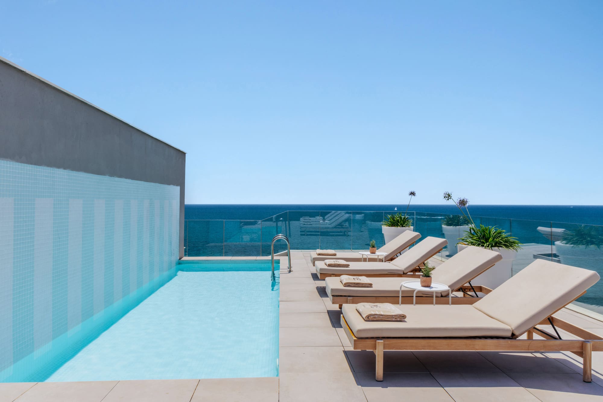 Rooftop infinity pool overlooking the ocean with sun loungers and blue sky.