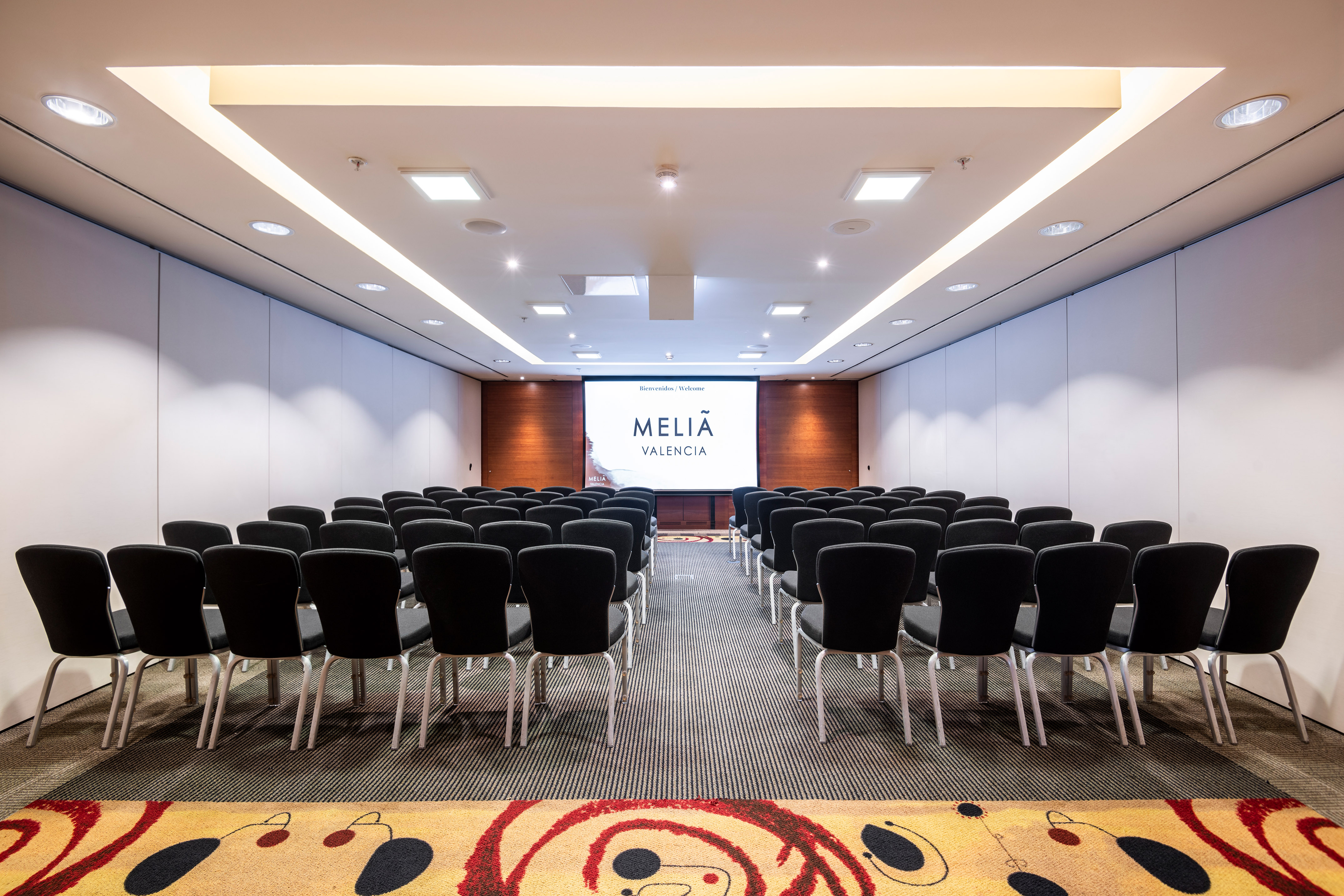Meliá Valencia conference room with rows of chairs and presentation screen.