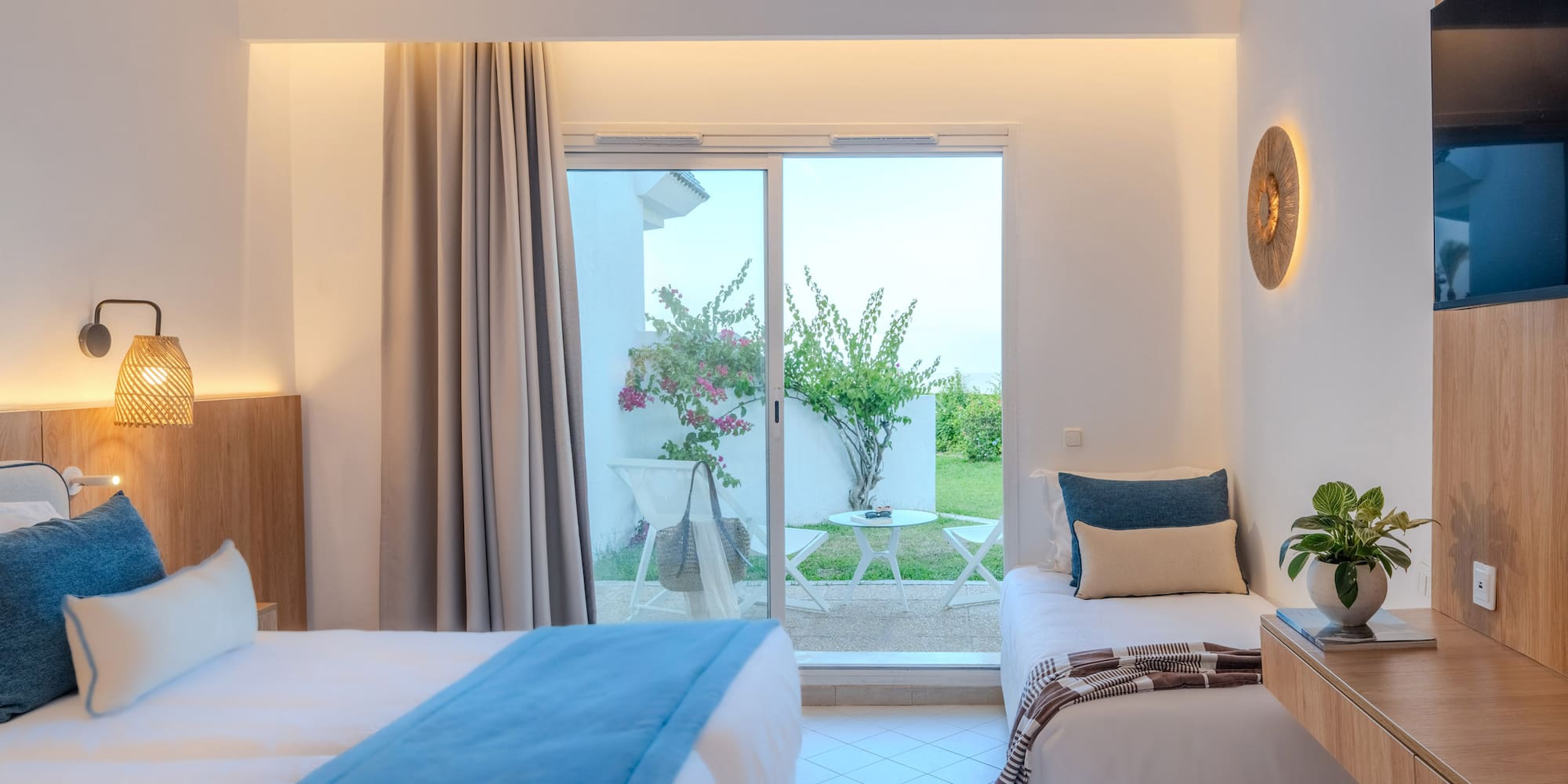 Modern hotel room with two beds, patio access, and lush garden view.