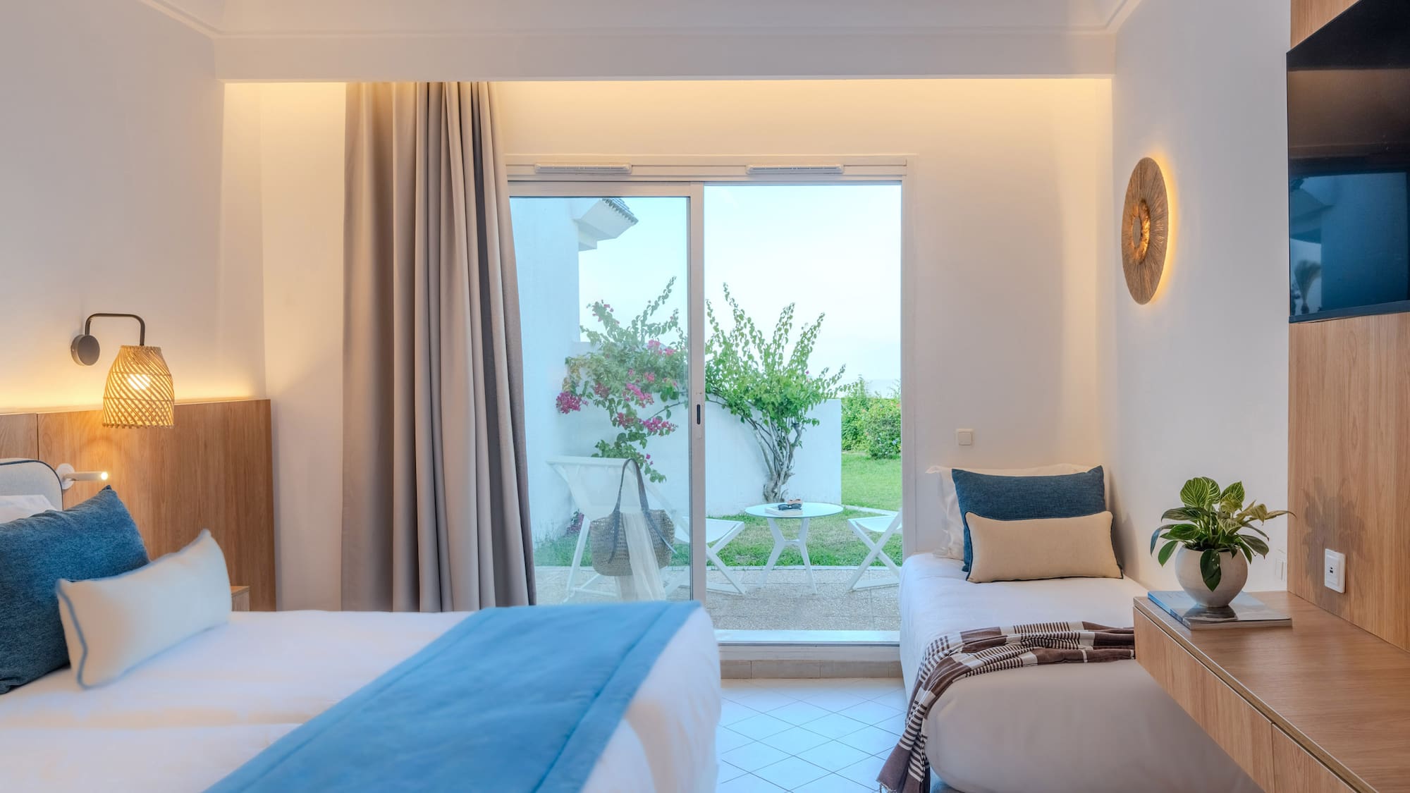 Modern hotel room with two beds, patio access, and lush garden view.