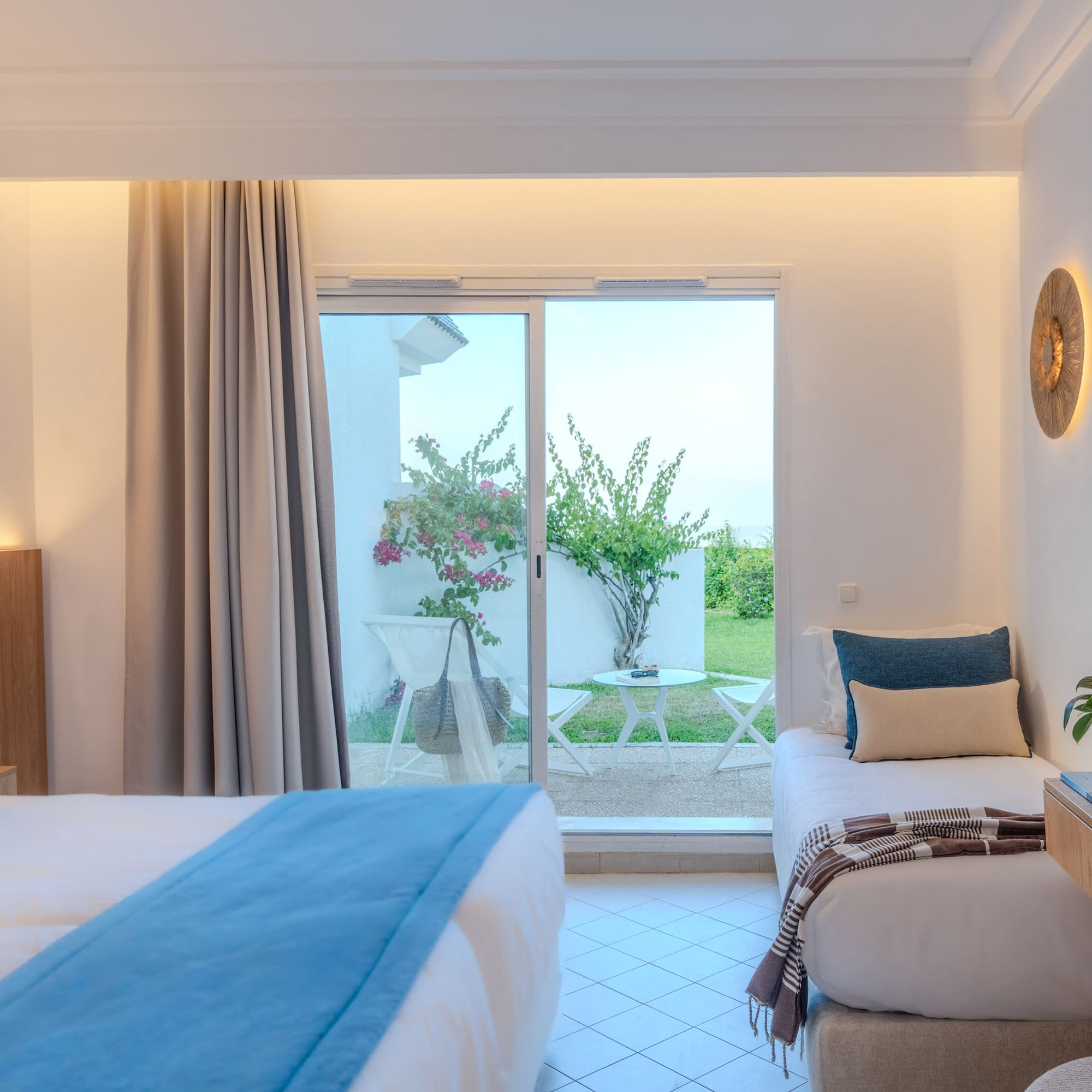 Modern hotel room with two beds, patio access, and lush garden view.