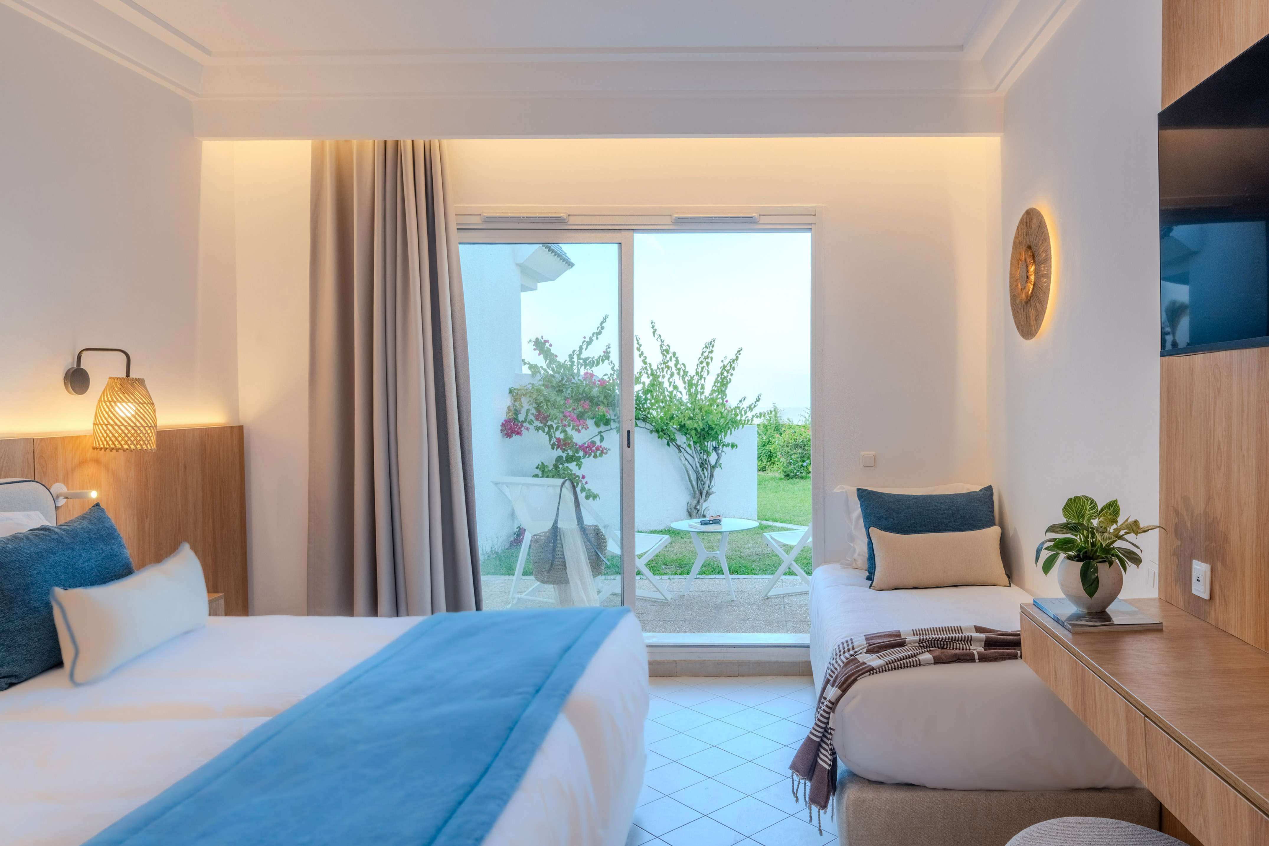 Modern hotel room with two beds, patio access, and lush garden view.