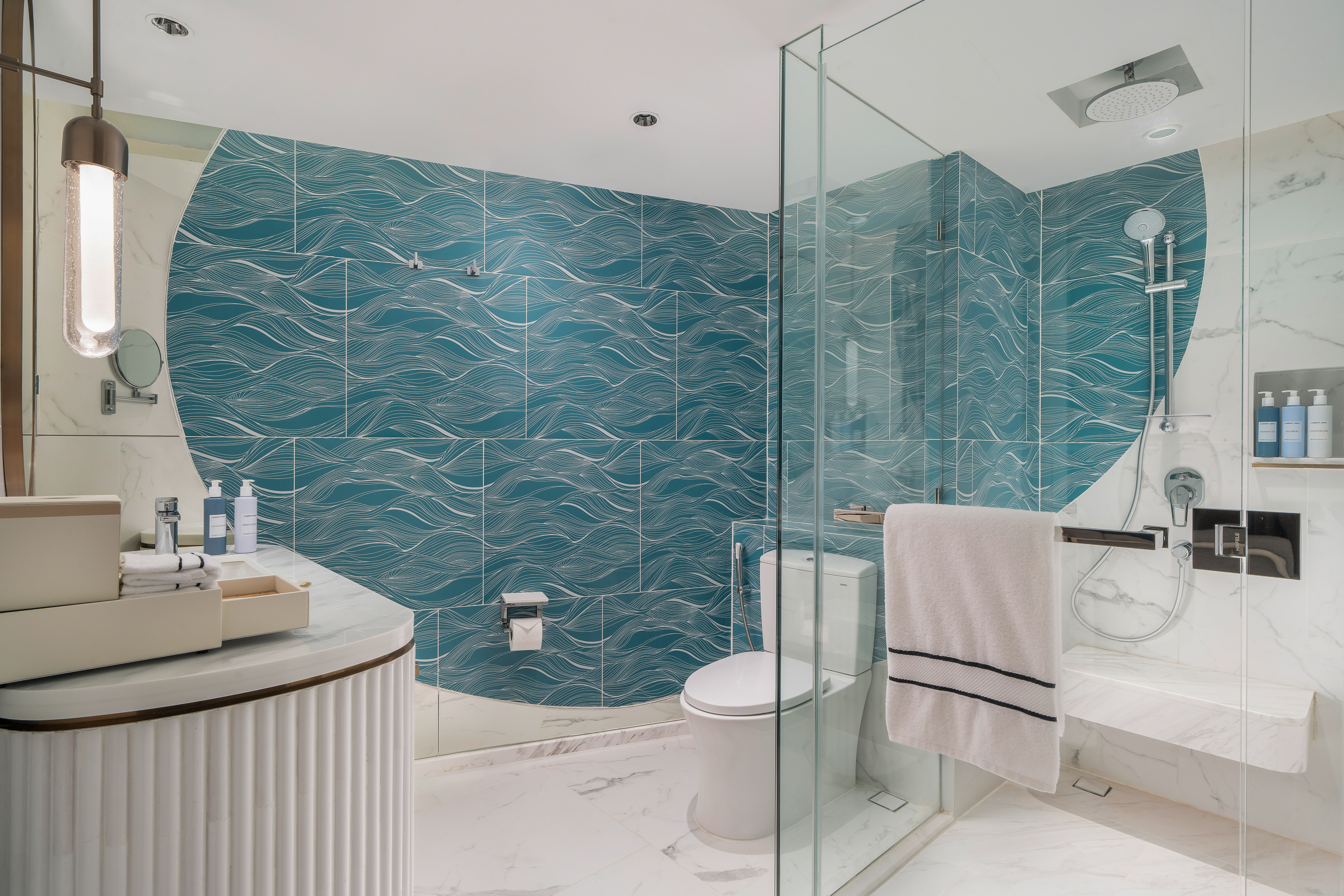 Modern bathroom with teal wave tiles, glass shower, toilet, and marble vanity.