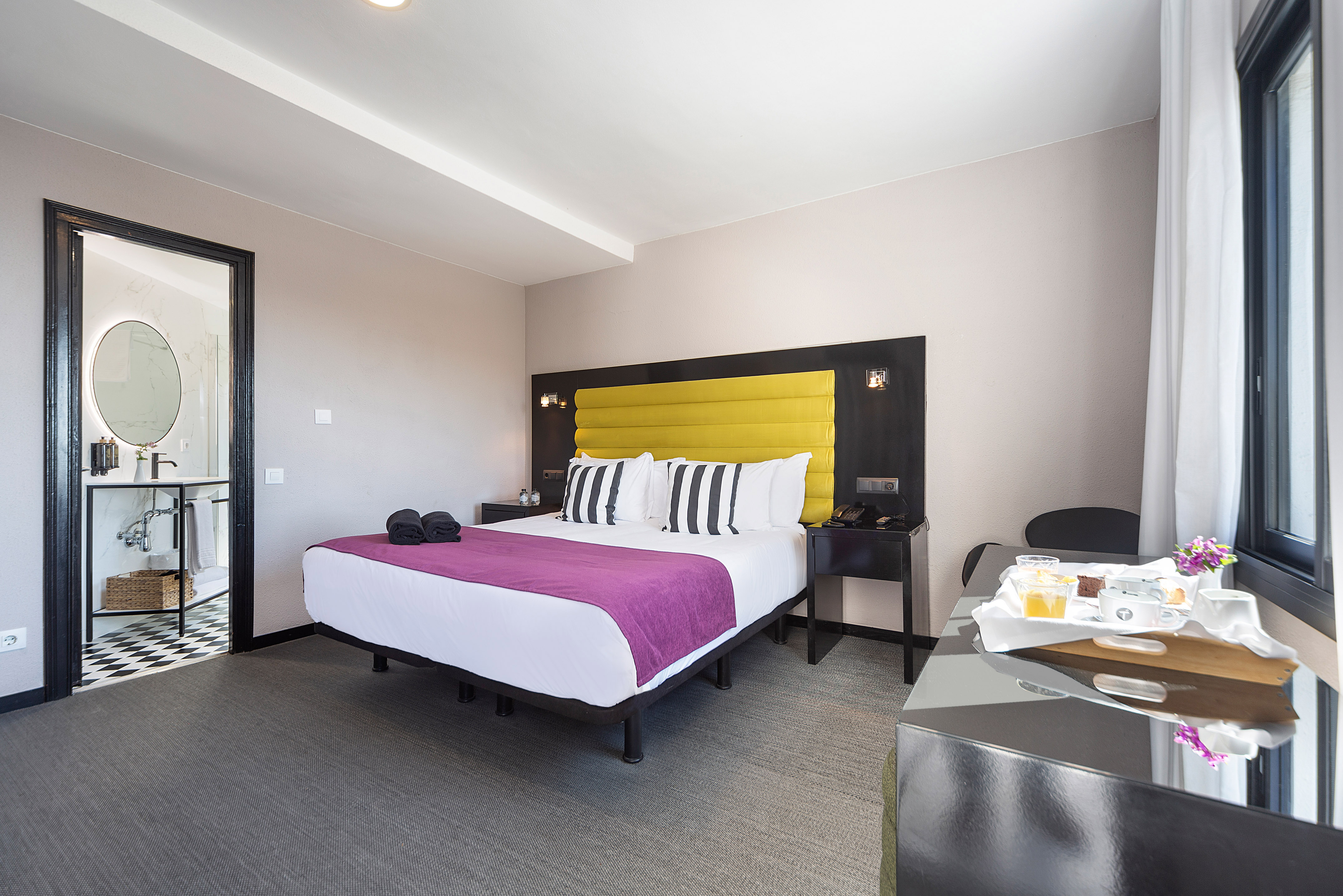 Hotel bedroom with yellow headboard, king bed, breakfast tray, and bathroom.