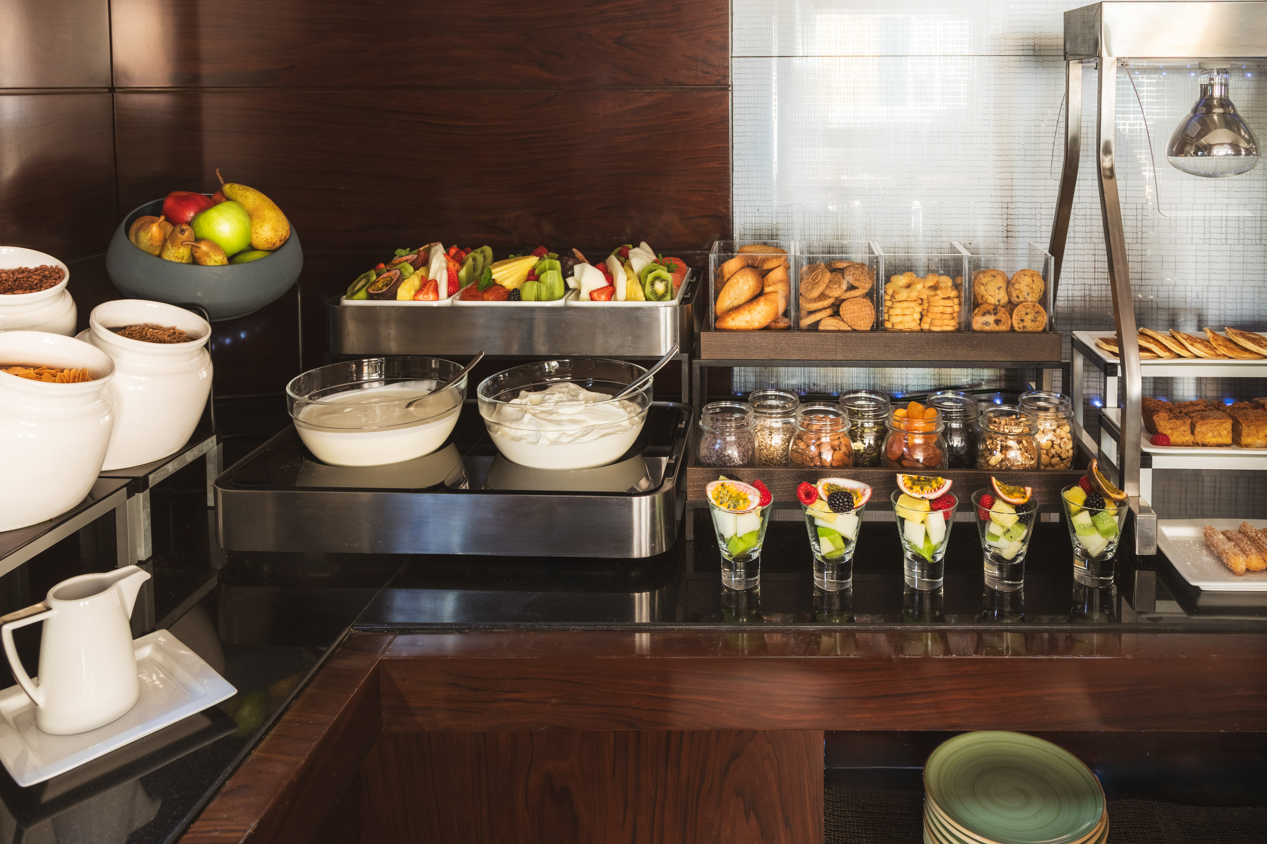 Continental breakfast buffet with fruit, yogurt, cereals, cookies, and hot pastries.
