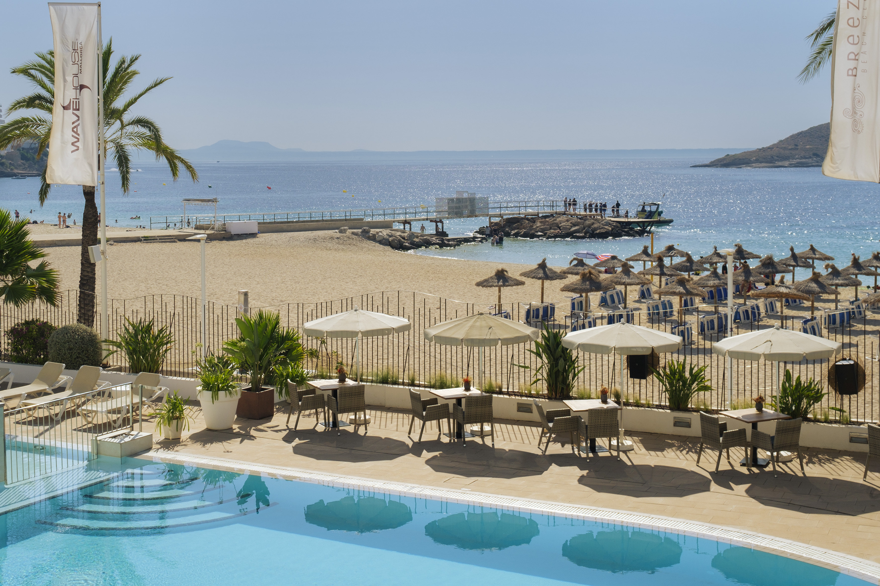 Sunny Mallorca beach resort with swimming pool, sandy beach, and clear ocean.