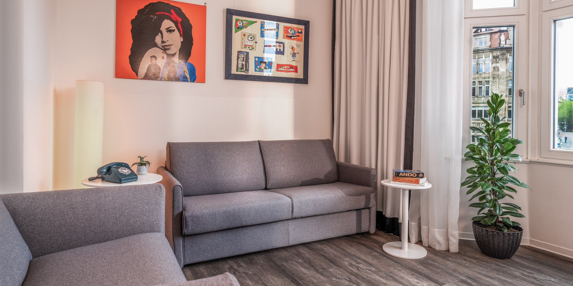 Grey sofa bed and armchair in modern living room with pop art and plant.