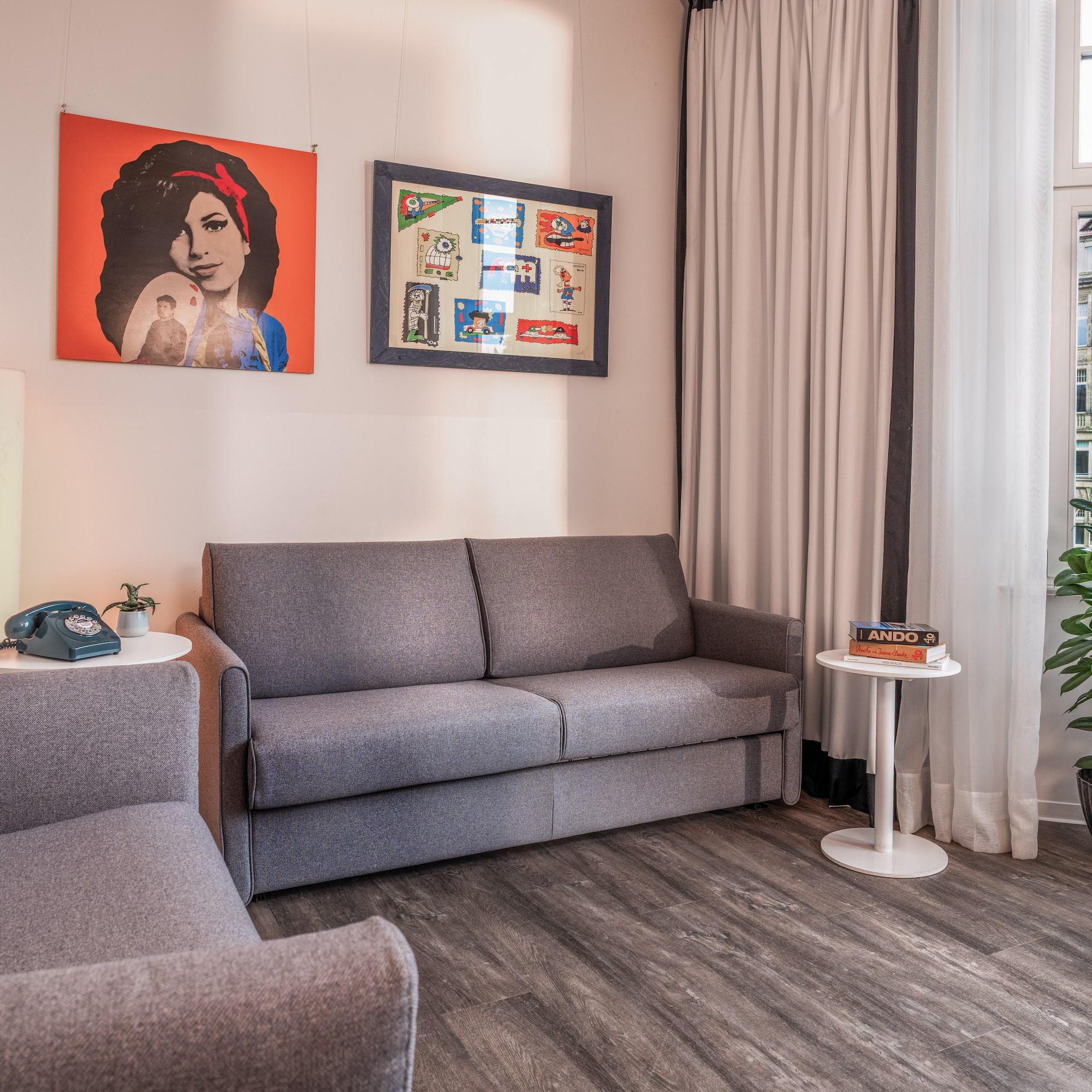 Grey sofa bed and armchair in modern living room with pop art and plant.