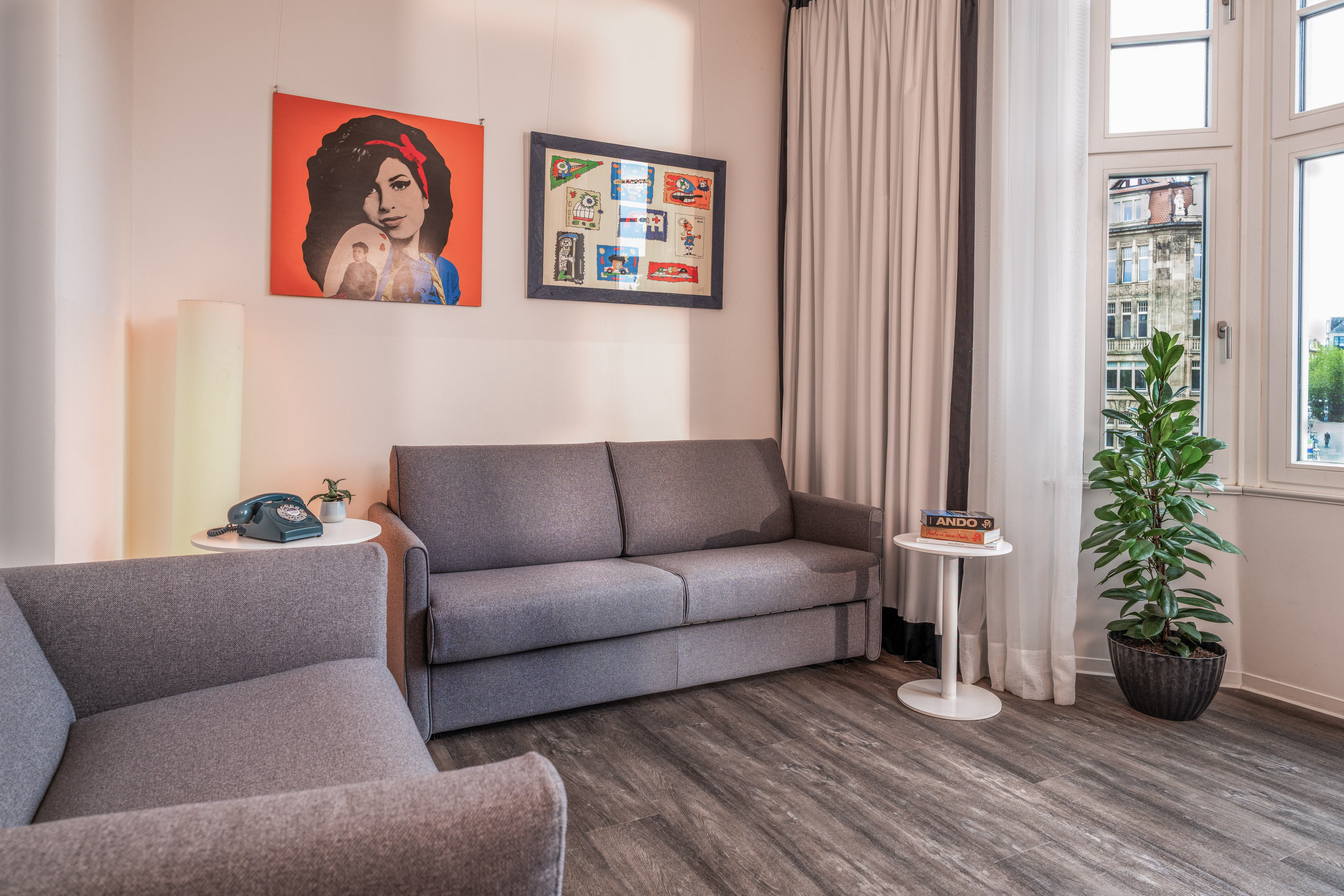 Grey sofa bed and armchair in modern living room with pop art and plant.