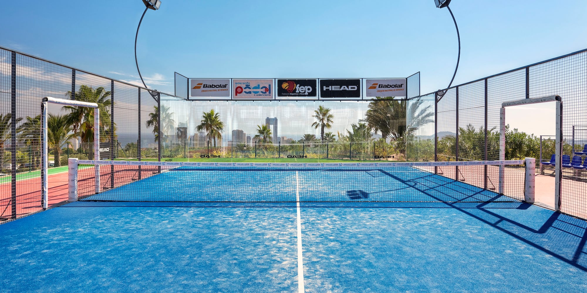 a tennis court with a fence and a city in the background