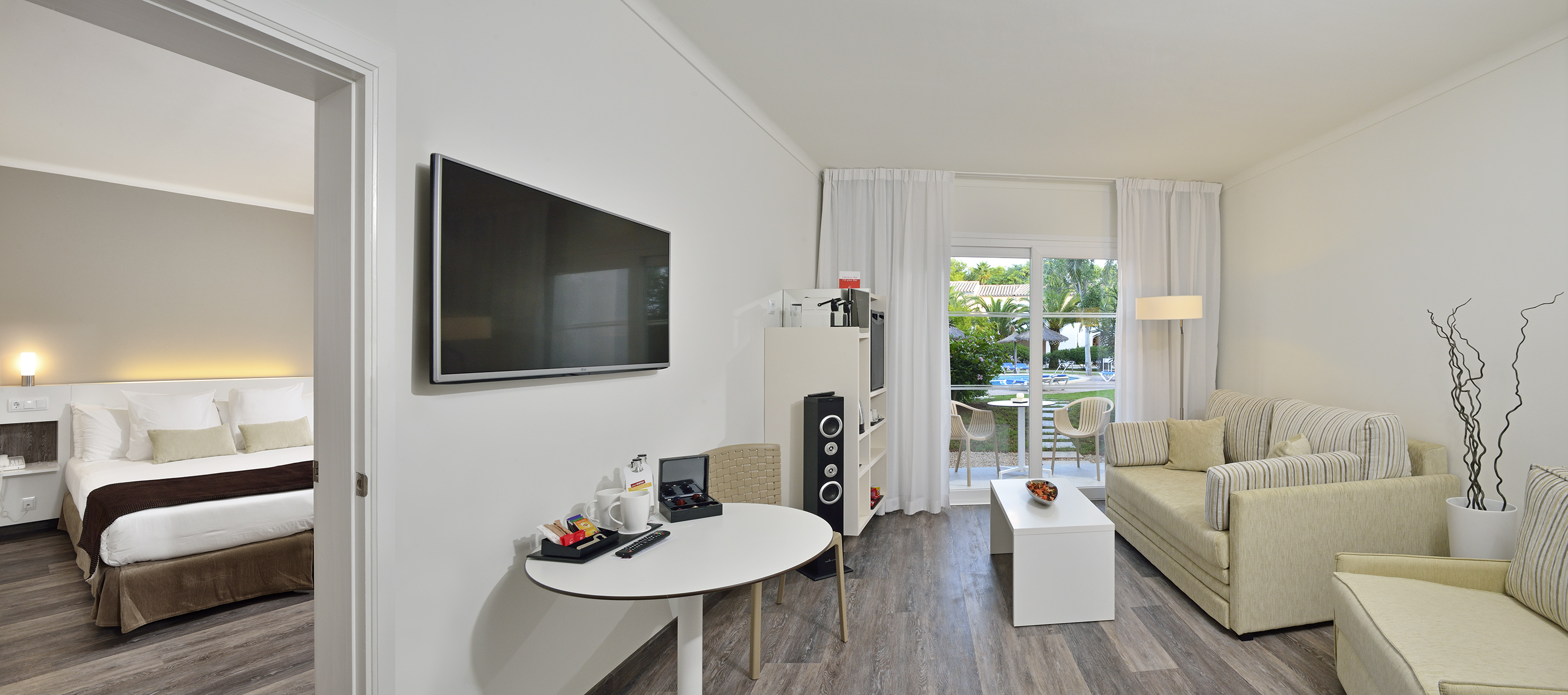 Modern hotel suite with living area, bedroom, and balcony overlooking a pool.