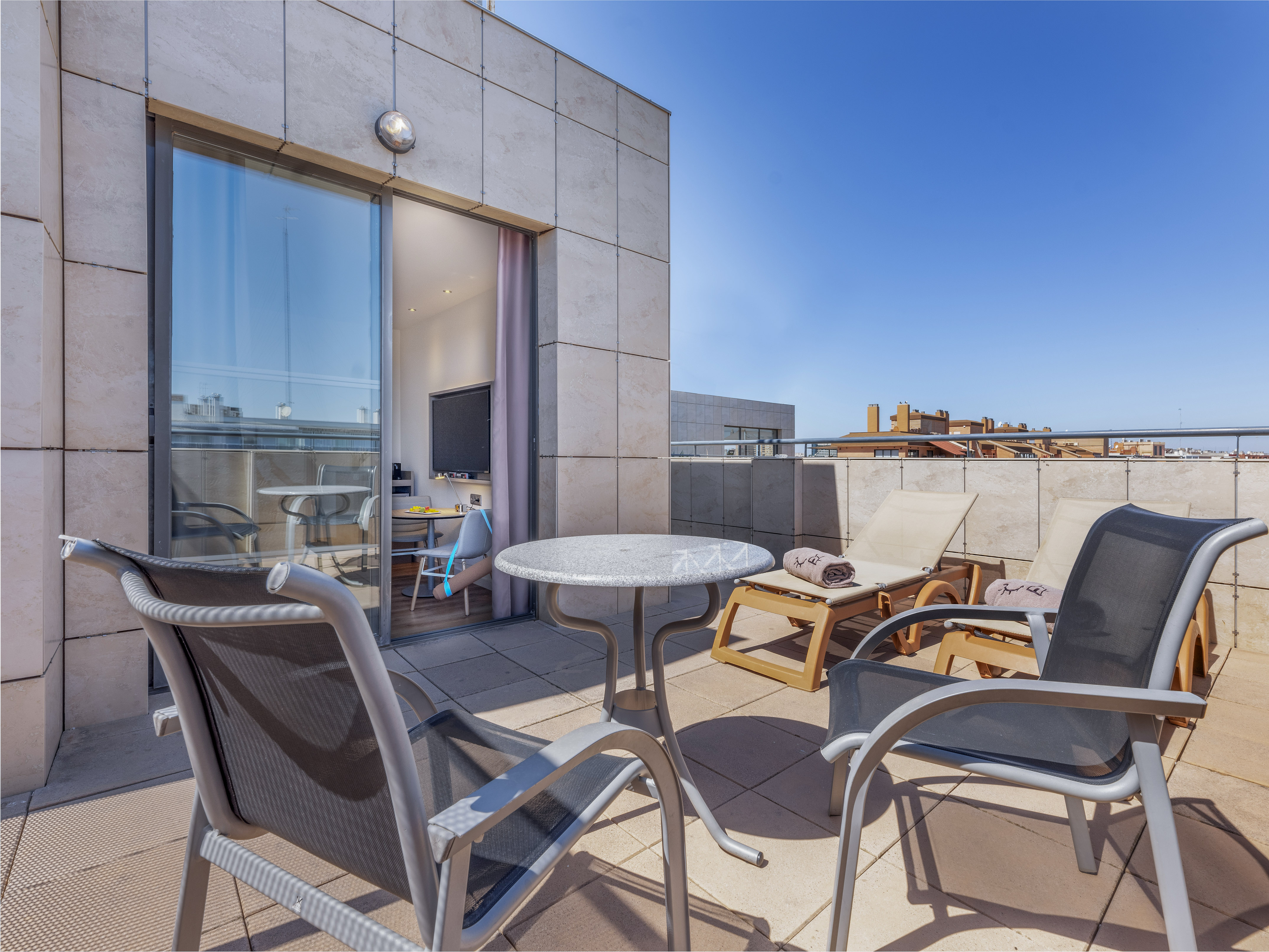 Sunny modern apartment terrace with outdoor lounge chairs and table.