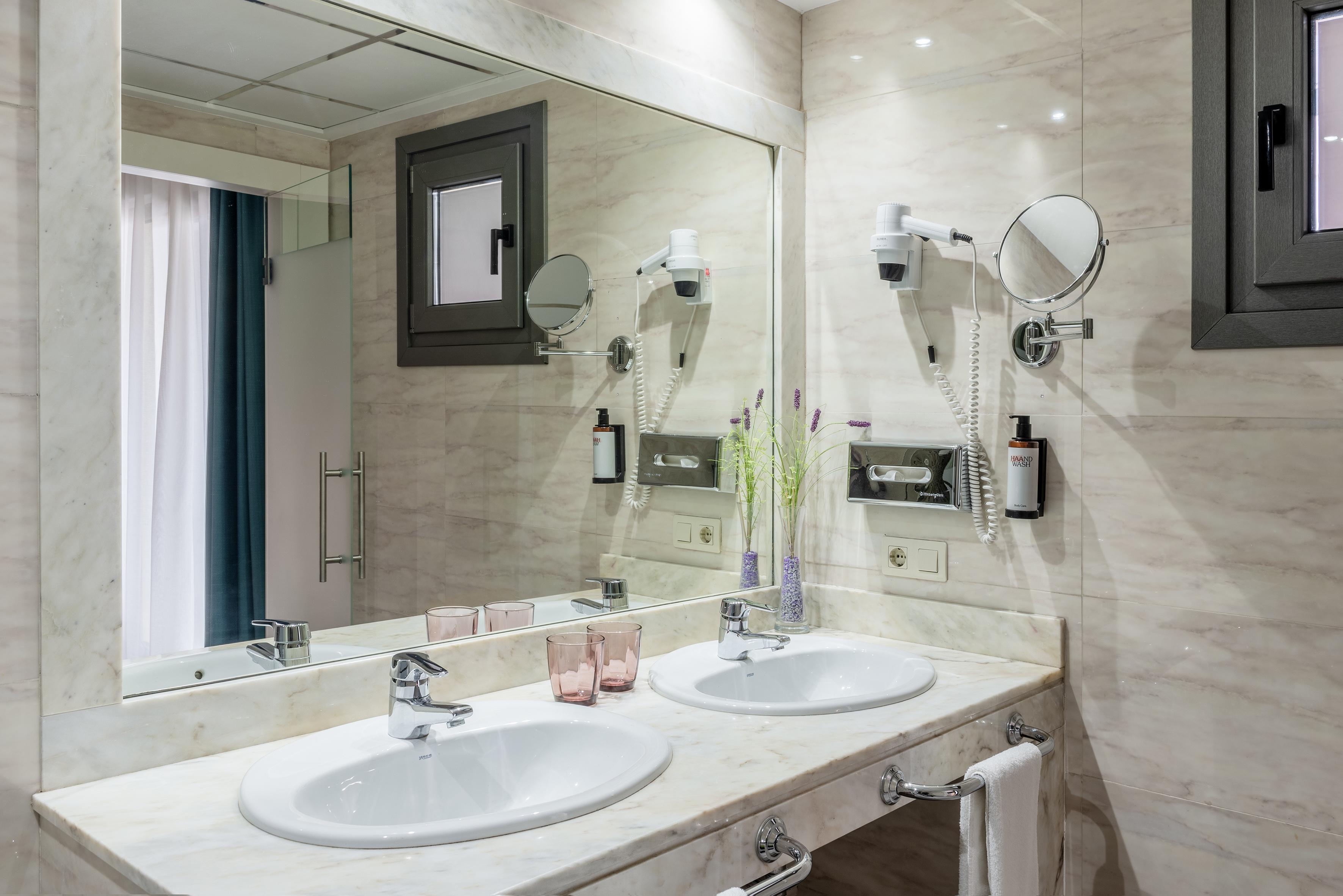 Hotel bathroom with marble double vanity, twin sinks, mirror, and amenities.
