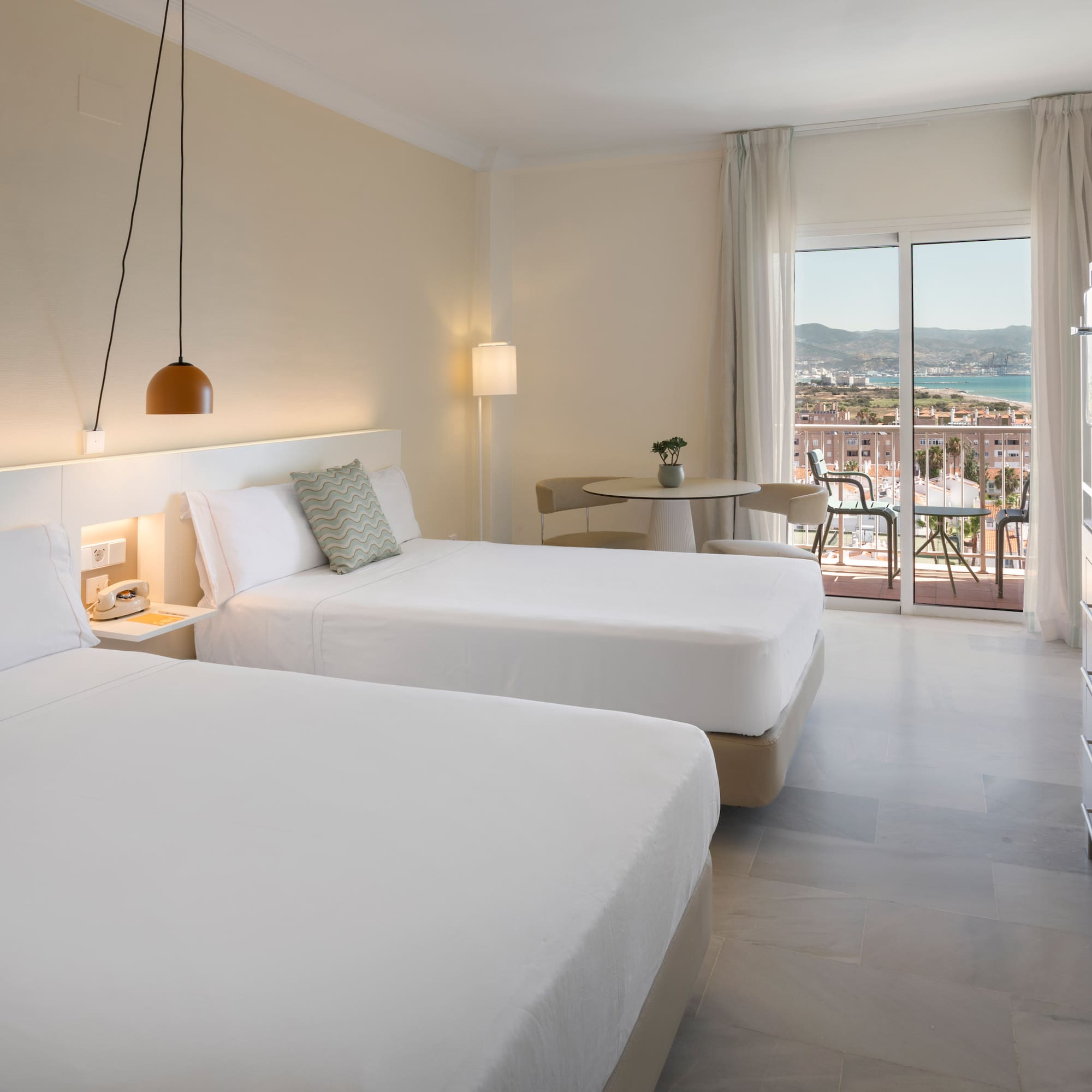 Habitación de hotel con dos camas, balcón y vistas al mar y ciudad.