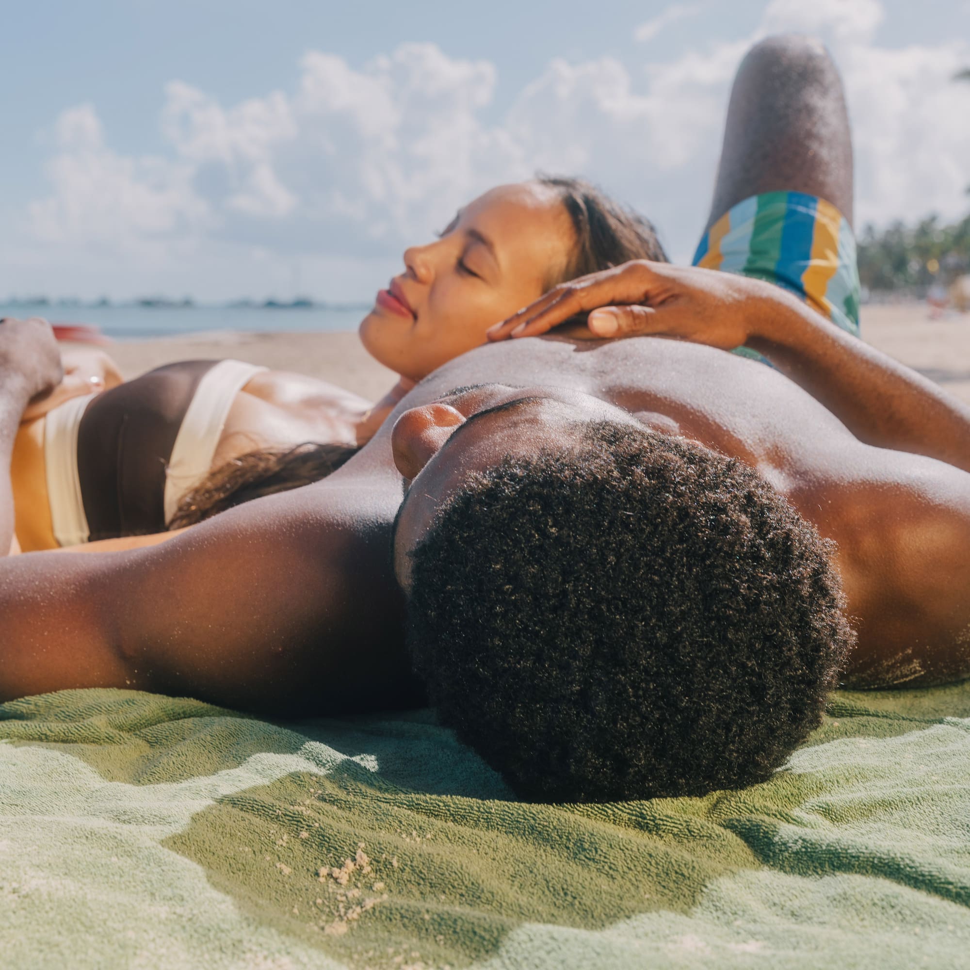 a man and woman lying on a towel on a beach