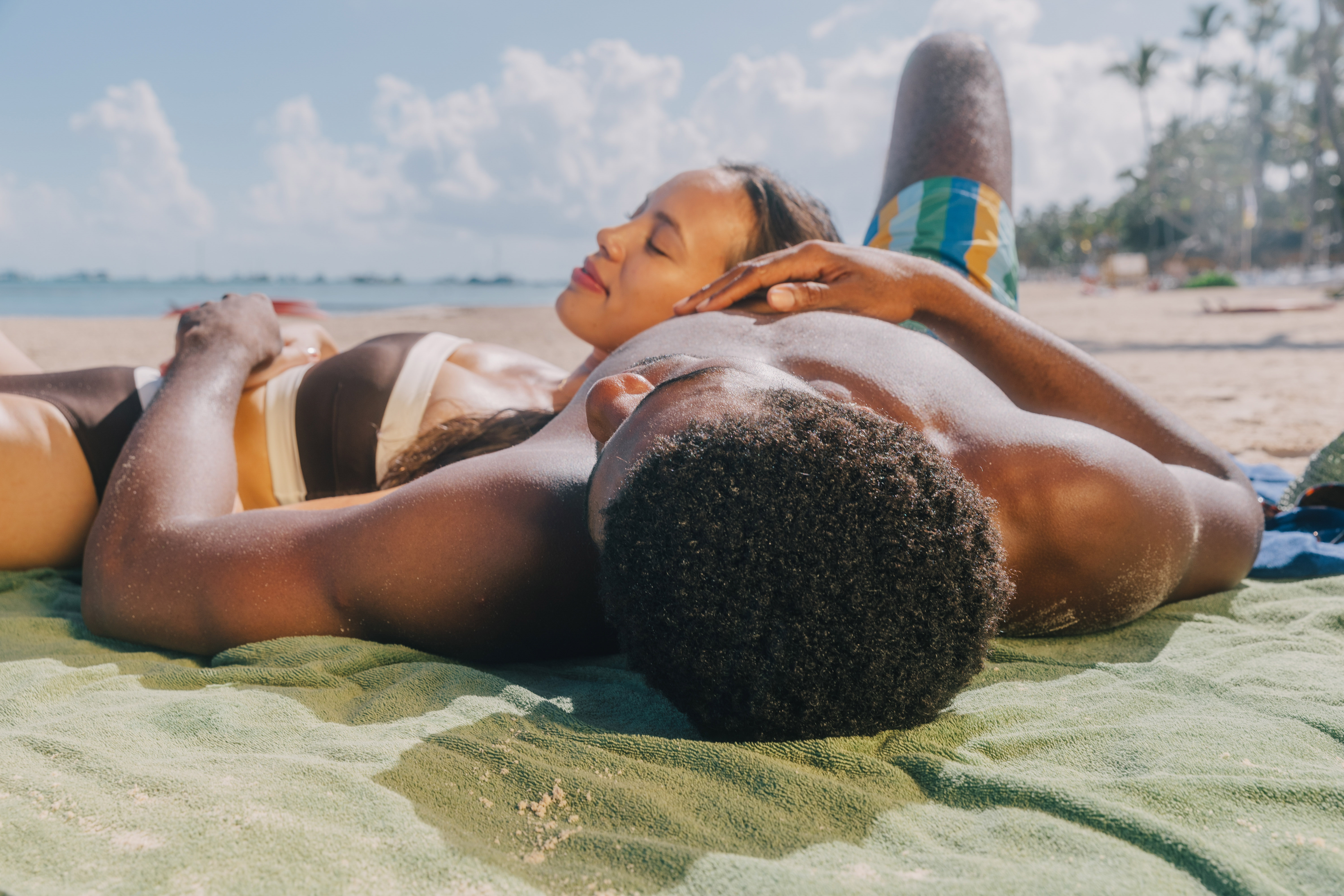 a man and woman lying on a towel on a beach