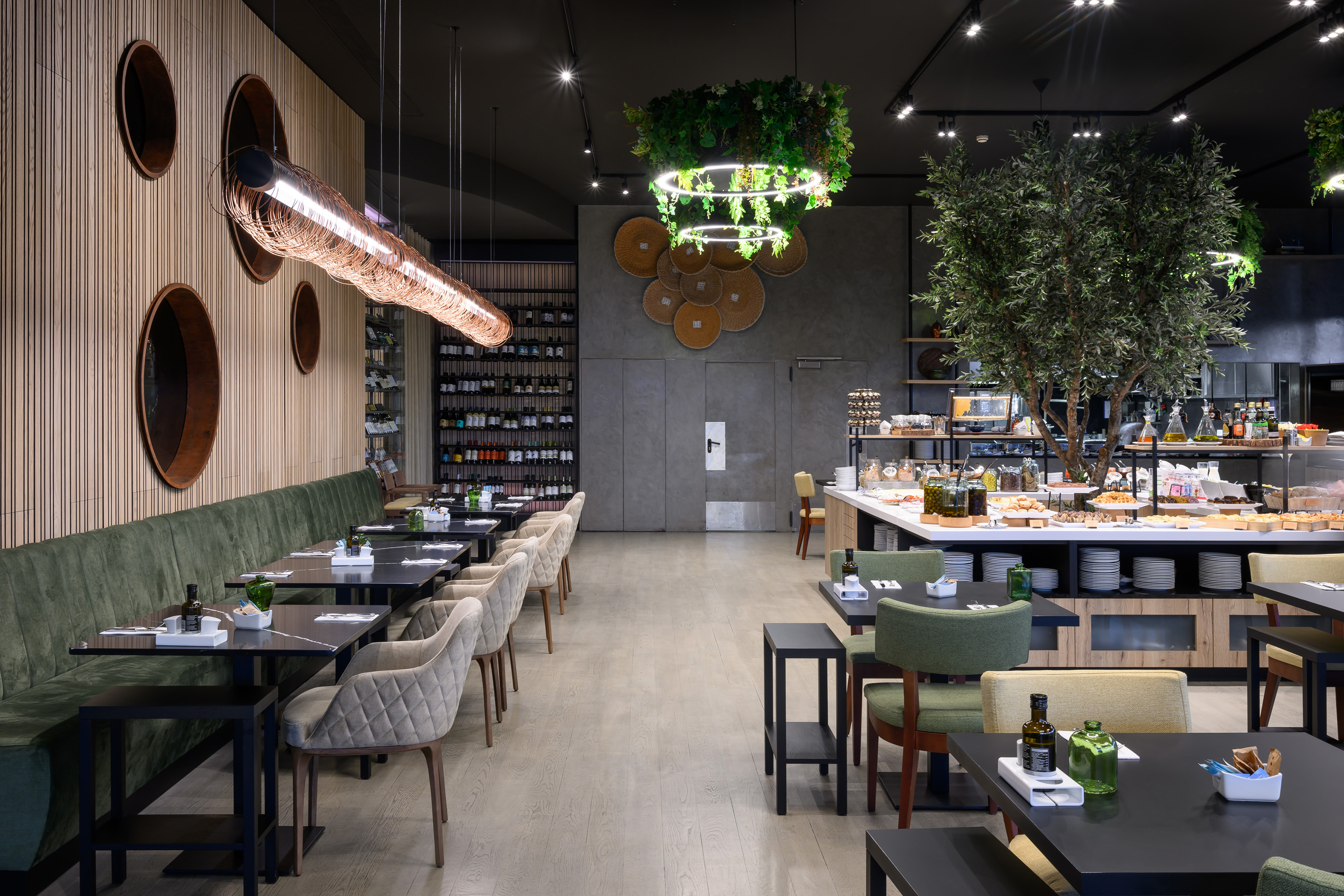 Contemporary hotel restaurant with breakfast buffet and decorative olive tree.