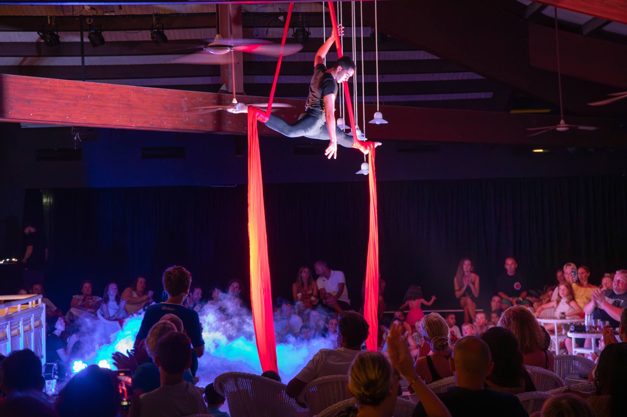 Aerialist performing splits on red silks above an audience at a show.