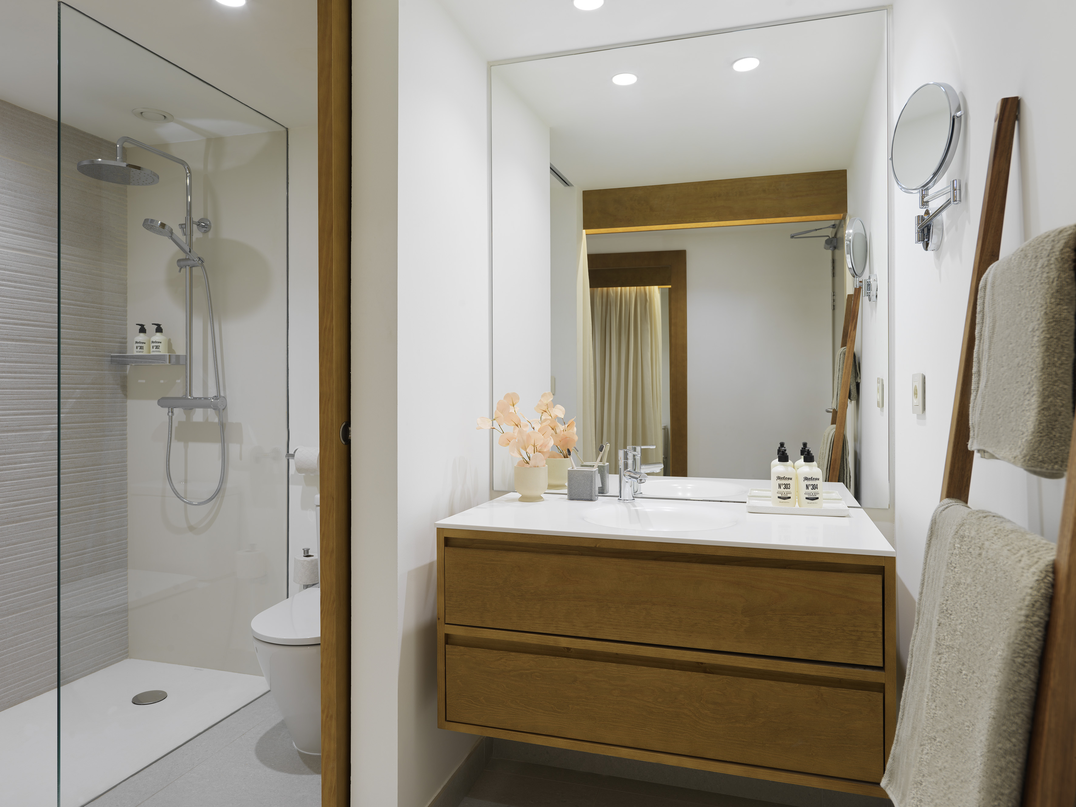 Modern bathroom with wood floating vanity, glass shower, and large mirror.