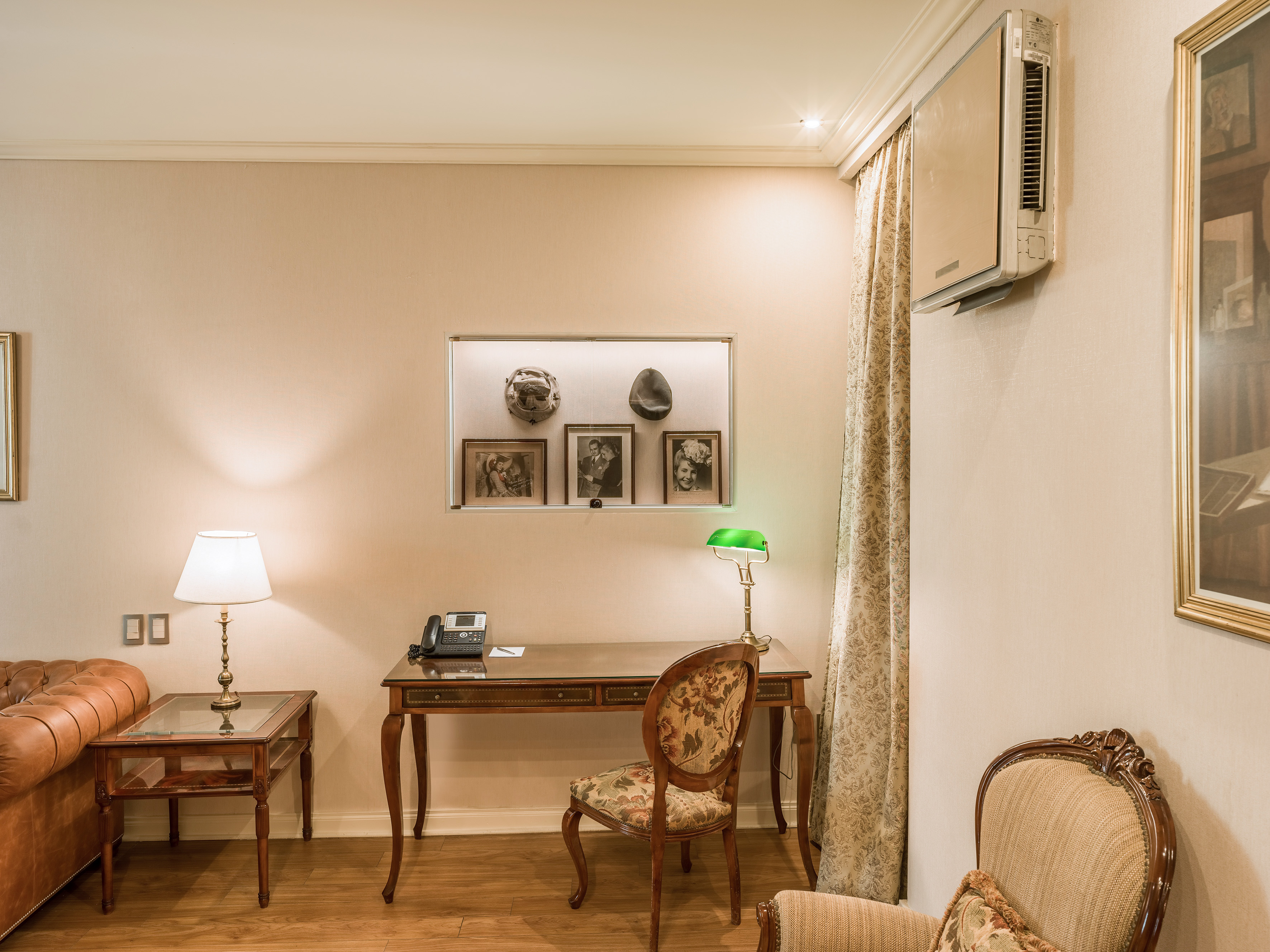 Elegant hotel room desk with green banker's lamp, vintage photos, and leather sofa.