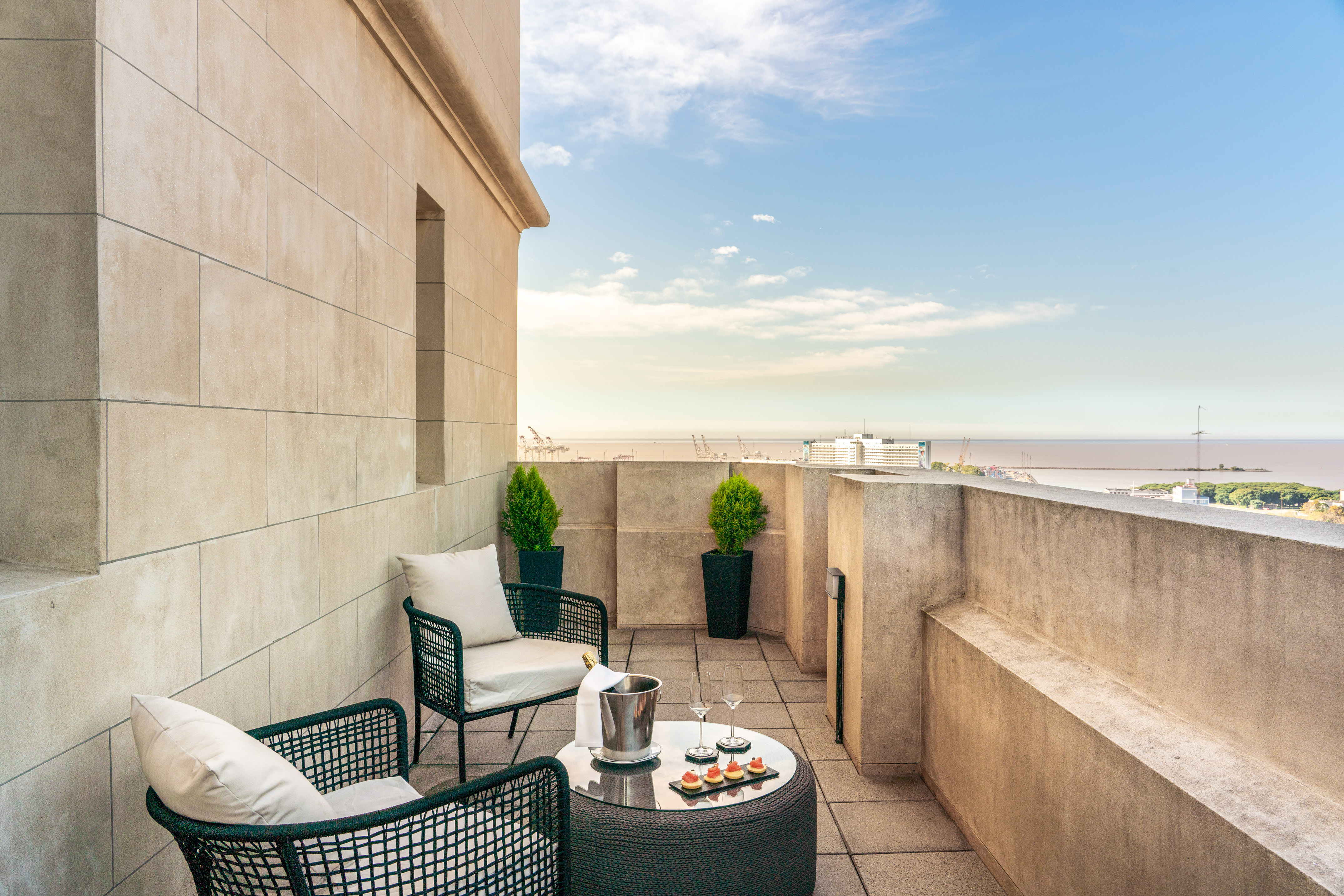 Hotel balcony with chairs, champagne, appetizers, and sea view.