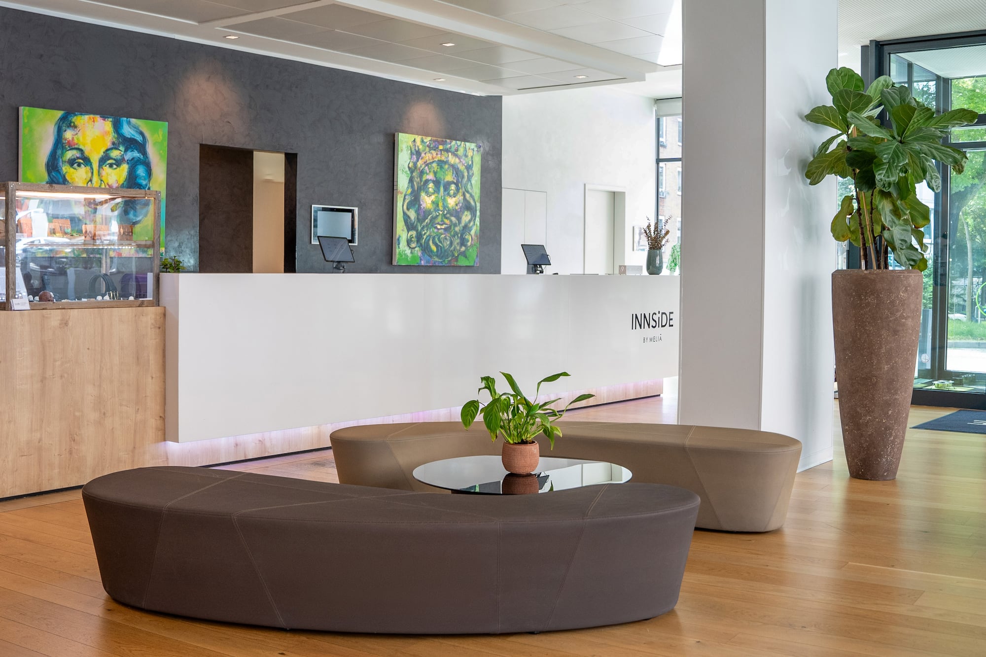 Modern INNSIDE hotel lobby with white reception desk, colorful art, and lounge area.