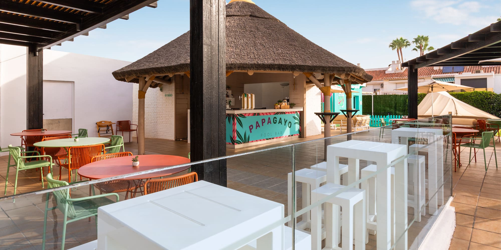 Terraza del Papagayo Pool Bar con quiosco de tejado de paja y mesas coloridas.